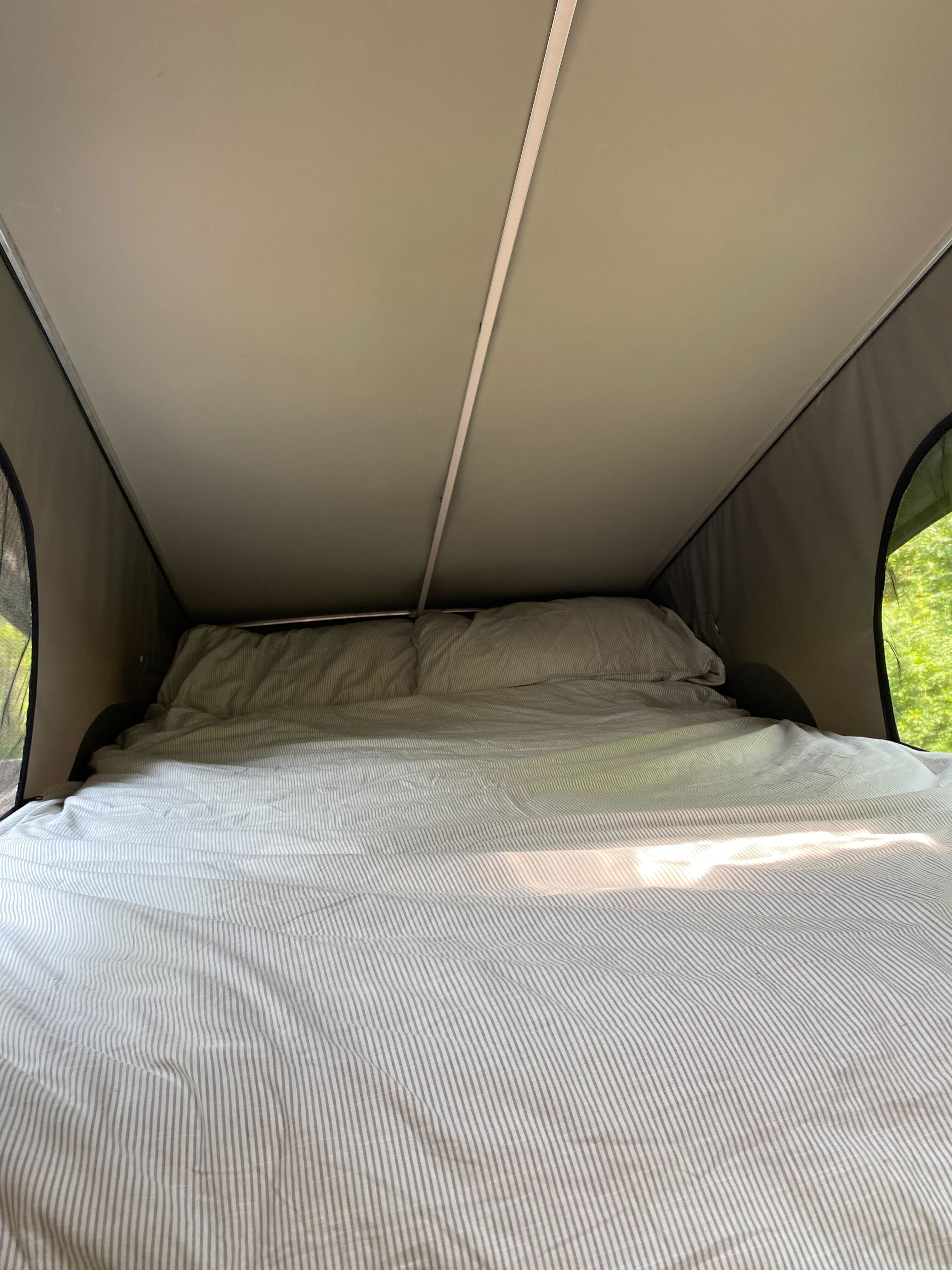 Cozy RV rental pop-top bed with striped bedding & view of nature. Perfect for camping comfort.. Other Other 2023