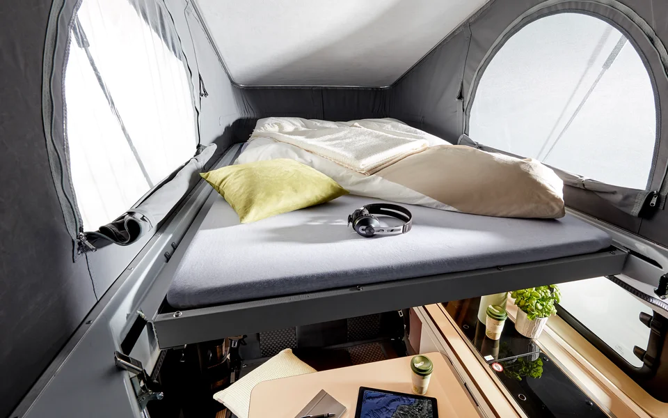 Cozy RV rental: pop-top bed with windows above a lower living area, showing bedding, pillows, and a table.. Bürstner COPA C530 2023