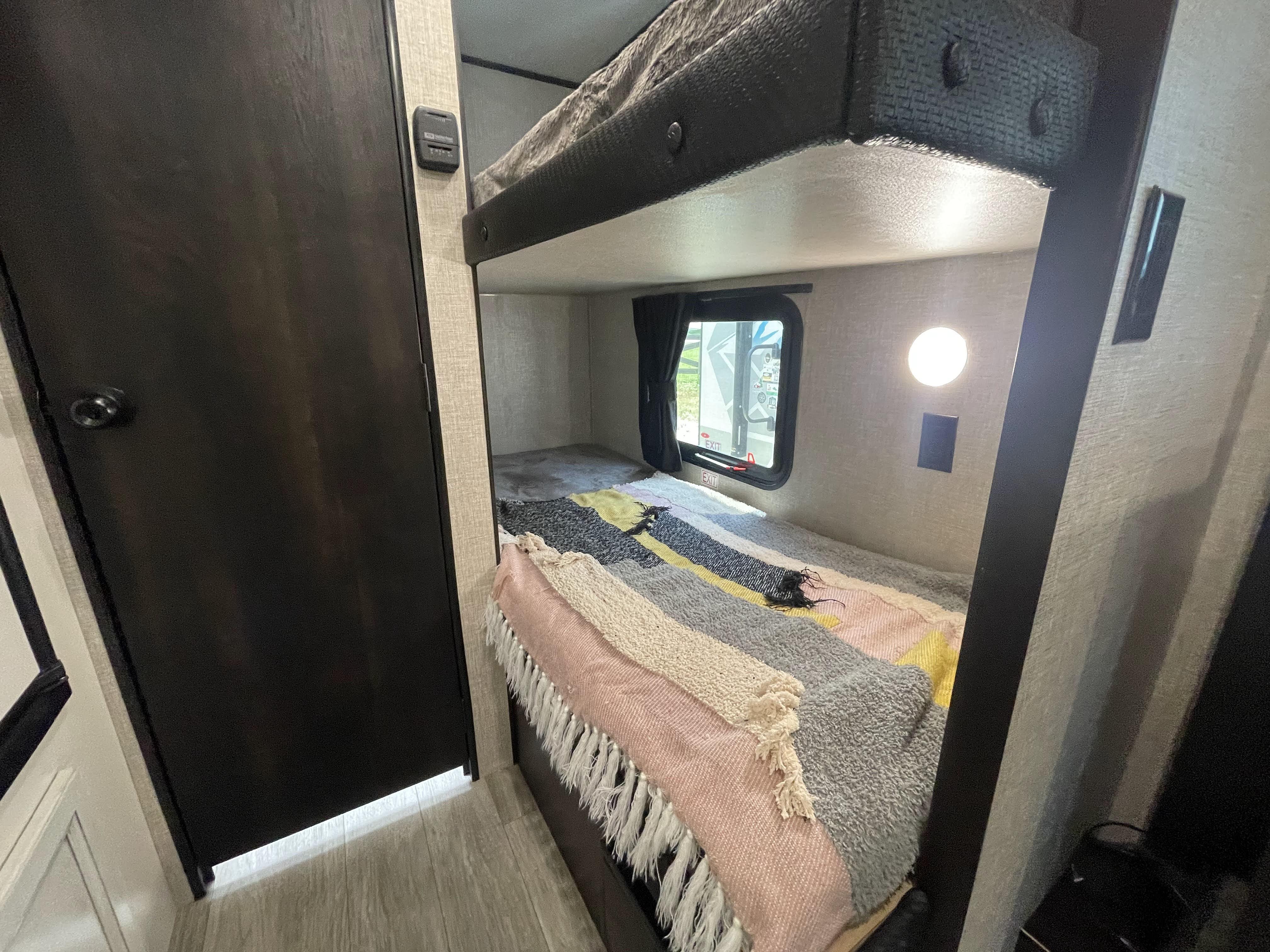 Cozy RV rental bunk beds, perfect for family travel. Features a lower bed with colorful blanket, upper bunk, and window.. Jayco Jay Flight 2022