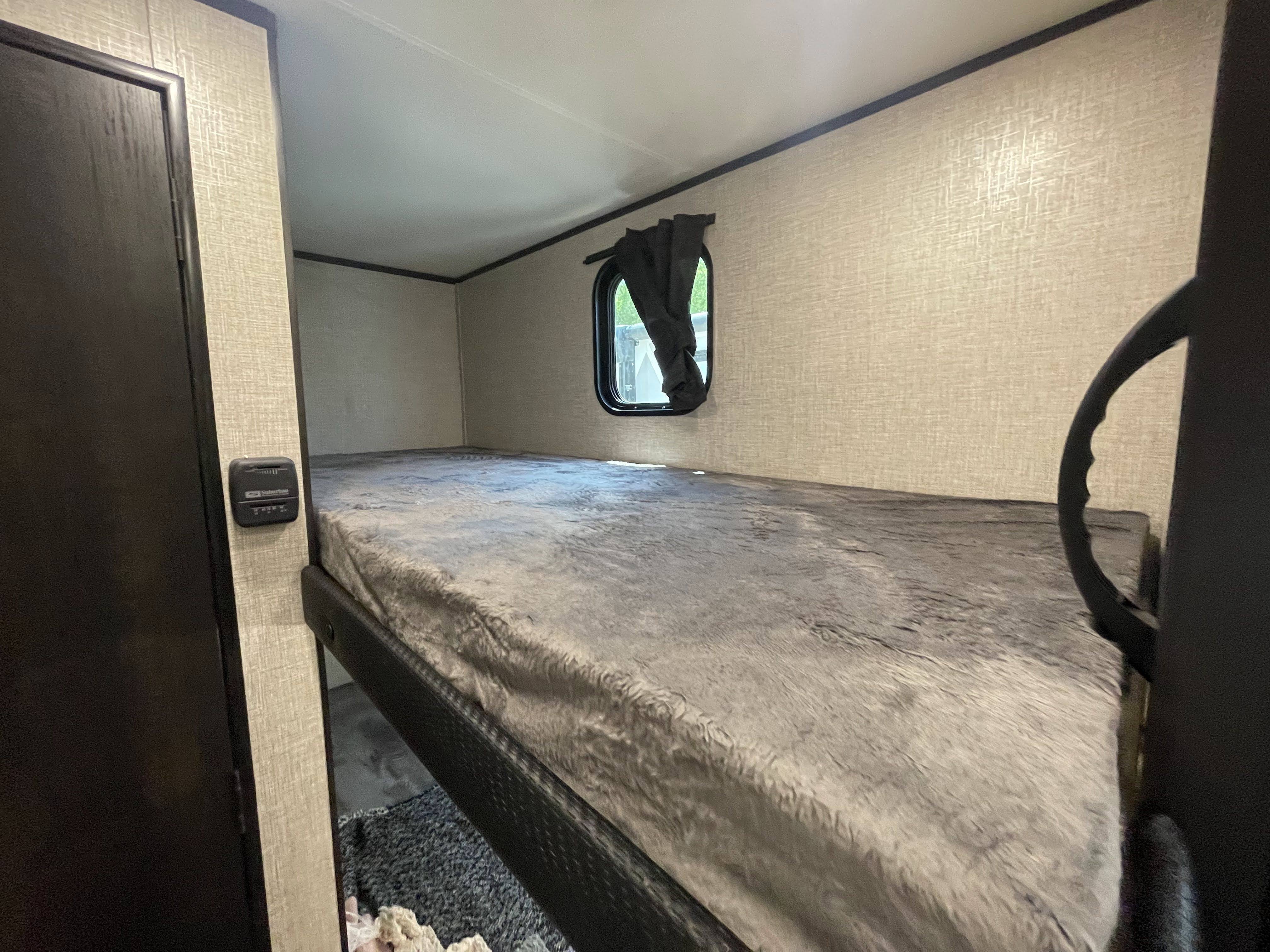 RV rental interior: A comfy bunk bed with a soft gray blanket, window, and thermostat on the wall. Ideal for travel.. Jayco Jay Flight 2022
