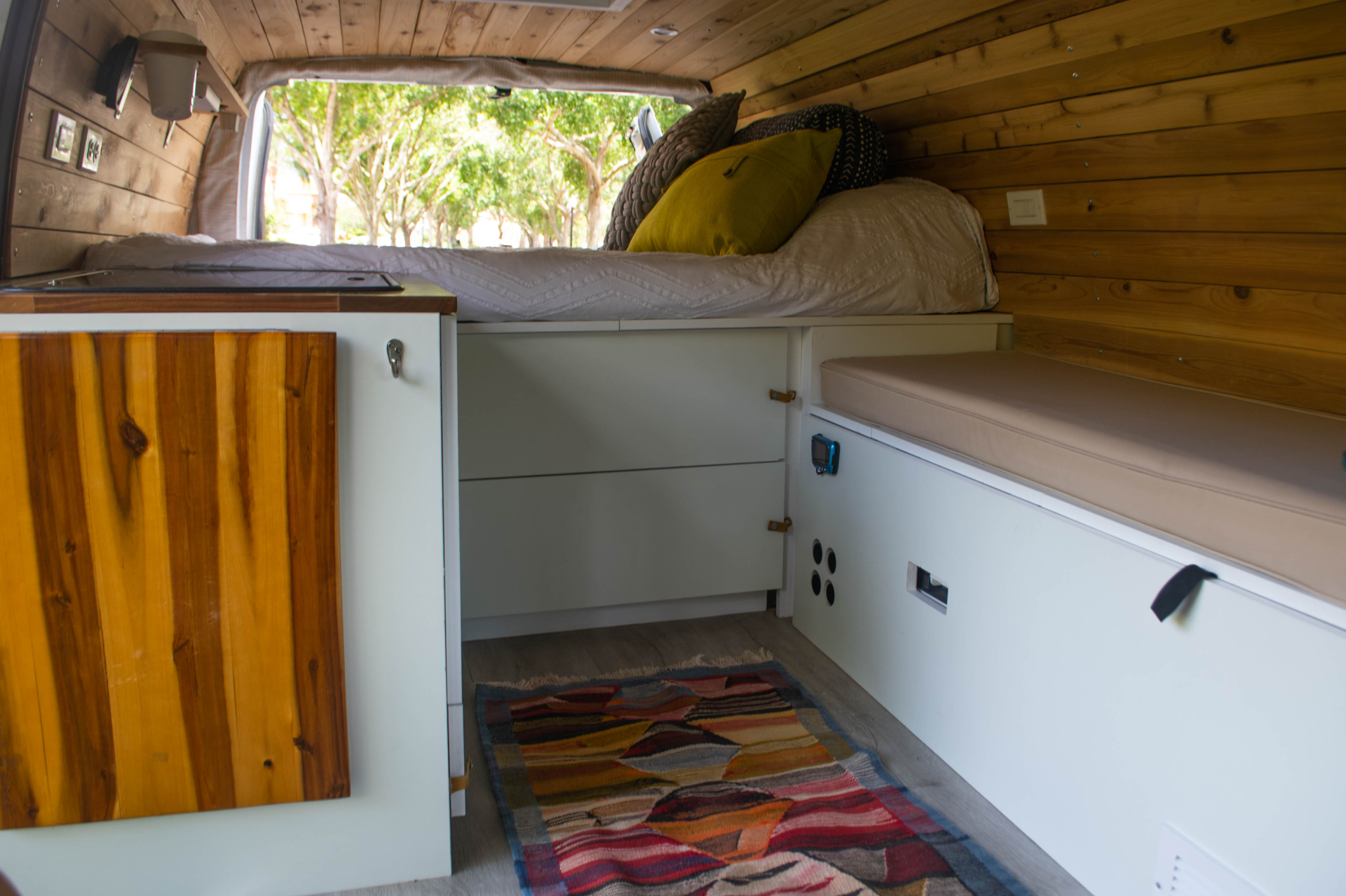 Inside this RV rental, find a cozy bed, compact kitchen, and storage cabinets amidst warm wooden walls and a colorful rug.. Ford Econoline 150 2010