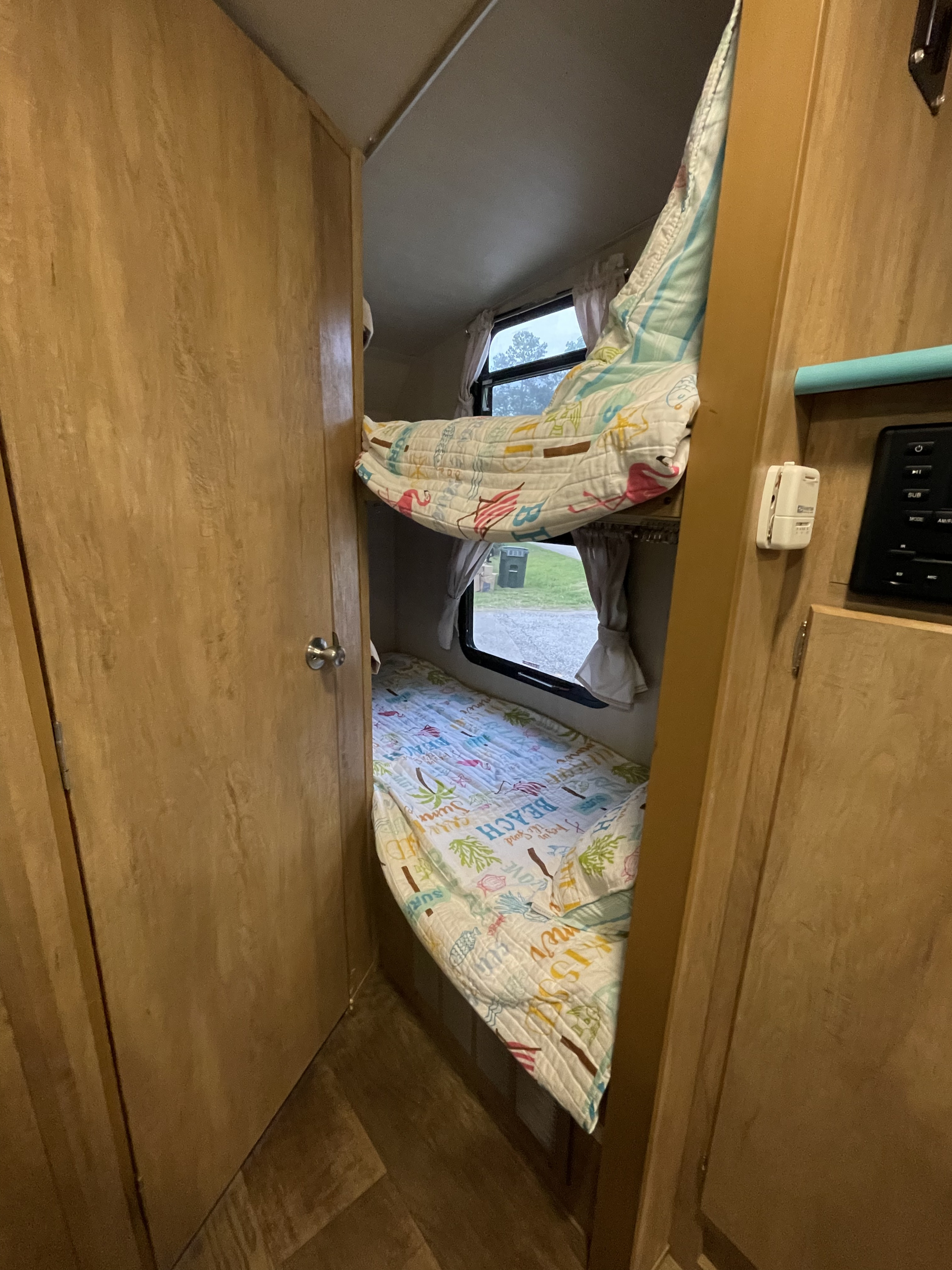 Cozy bunk beds inside an RV rental, offering comfortable sleeping for family camping trips. Windows show the outdoors.. Gulf Stream Vintage Cruiser 2018