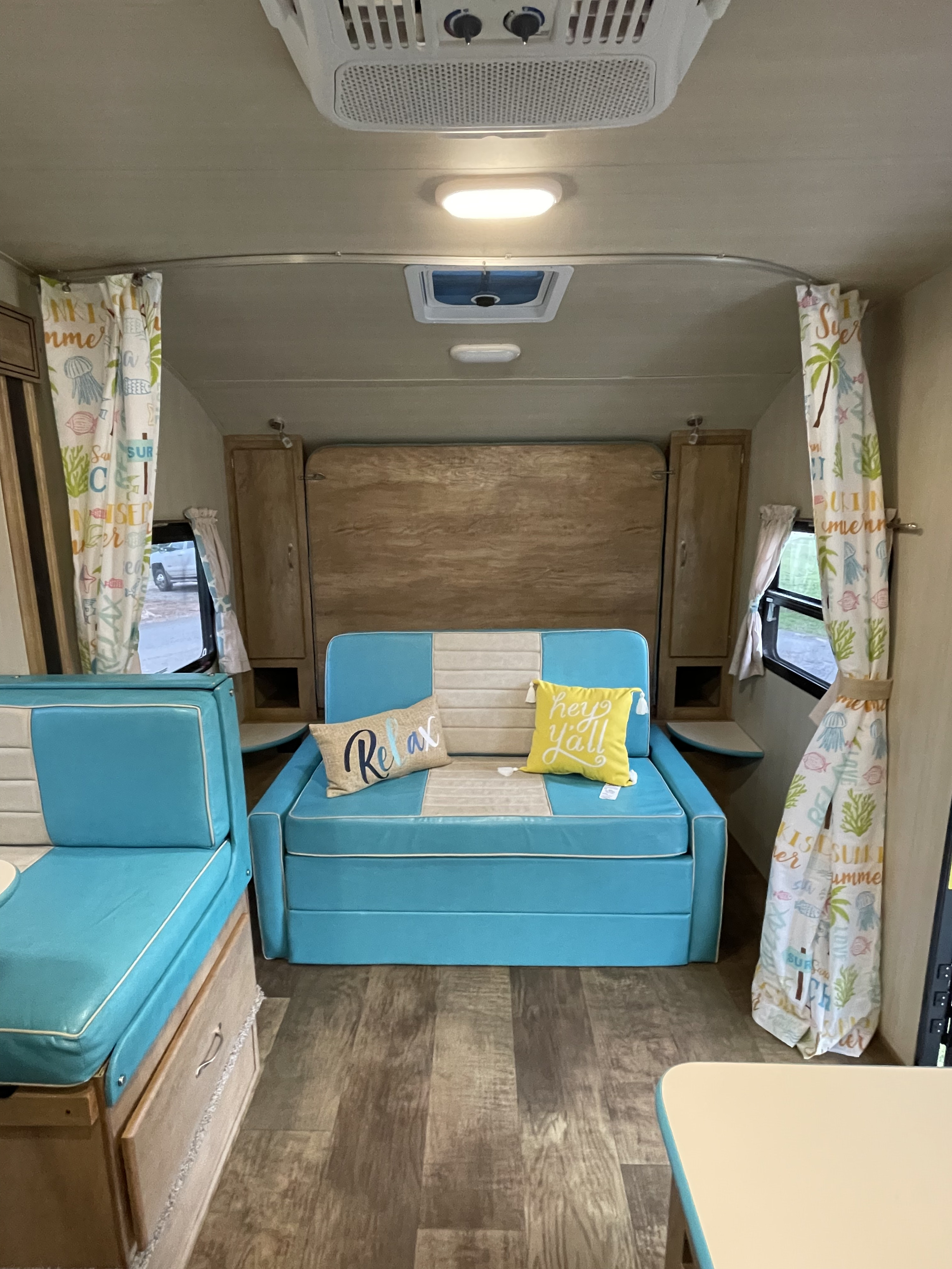 Bright blue sofa/bed and wood tones in a compact RV rental interior, complete with cheerful summer-themed curtains.. Gulf Stream Vintage Cruiser 2018