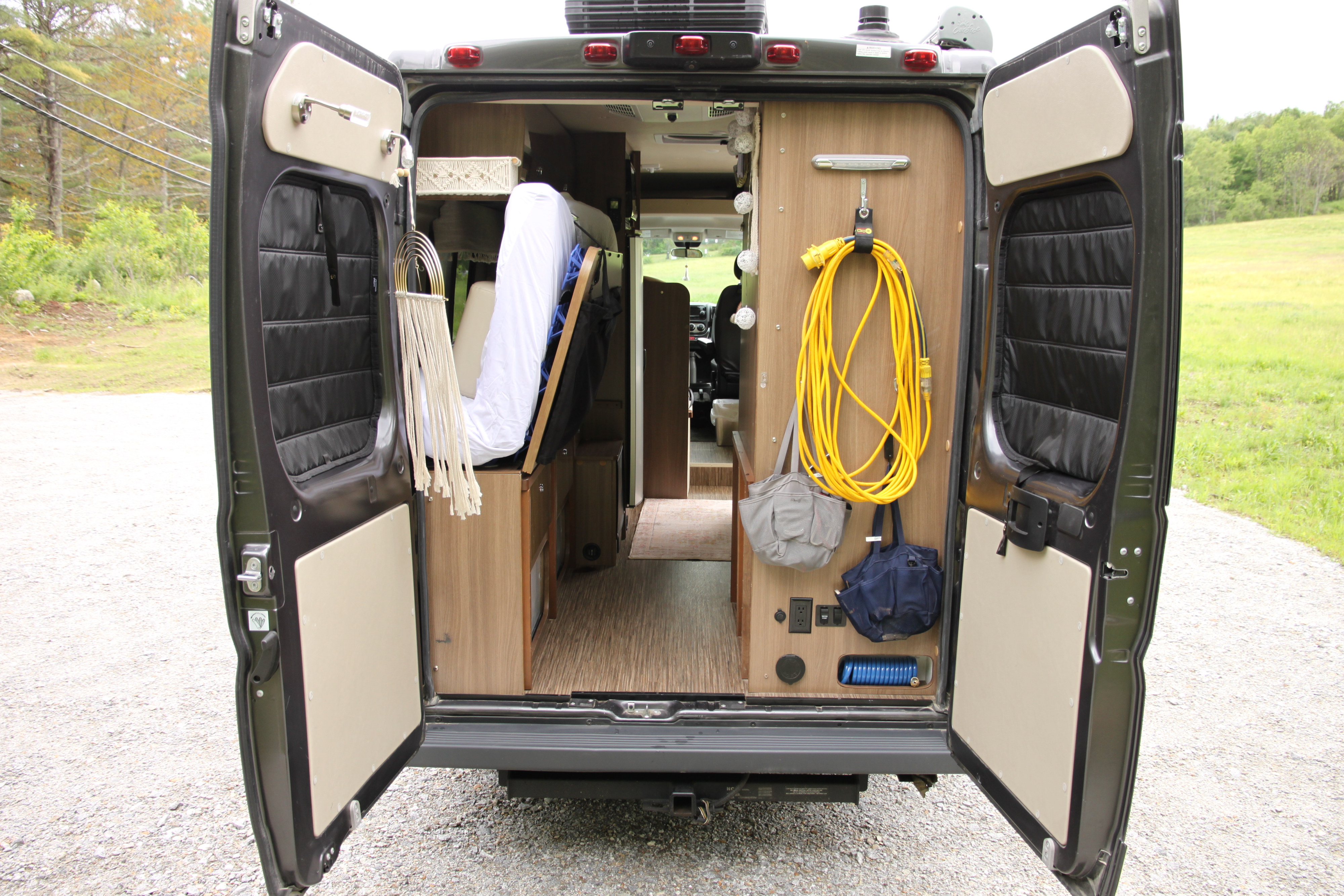RV rental rear interior, with open doors showcasing organized storage: power cord, utility bags, and interior cabin.. Winnebago Travato 2017