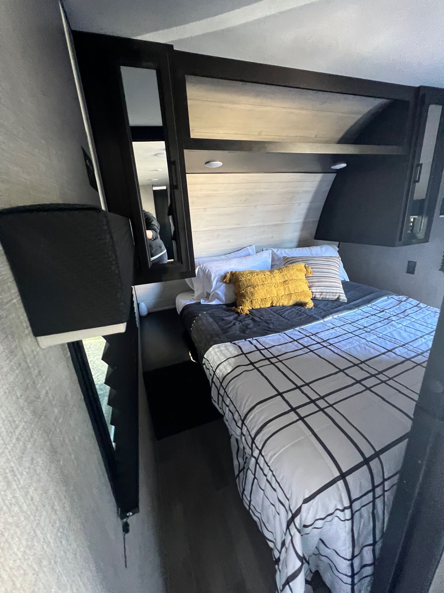 This comfortable RV rental bedroom features plaid bedding, dark overhead cabinets, and a mirror reflecting the interior.. Jayco Jay Flight 267BH 2023