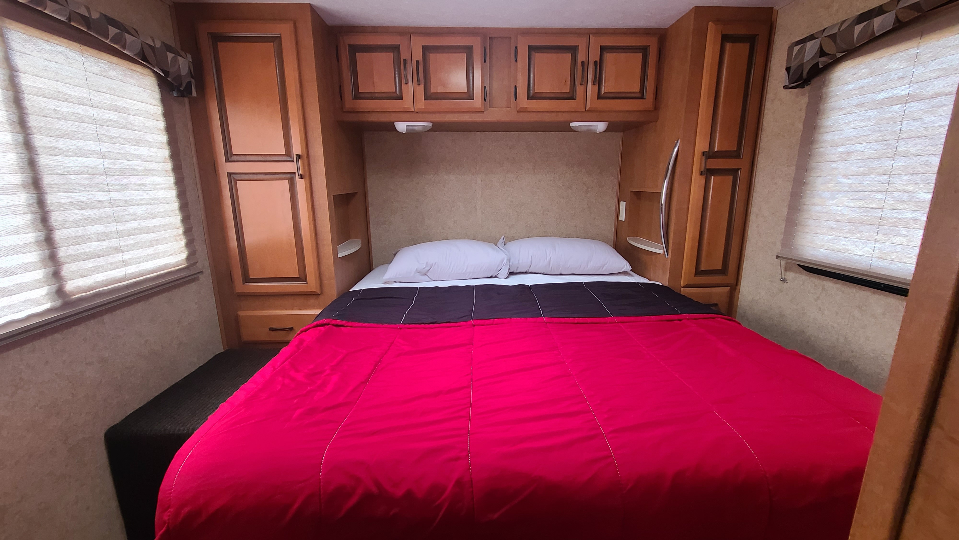 Inviting RV rental bedroom with a comfy bed, red comforter, white pillows, and wood storage cabinets.. Forest River Sunseeker 2011