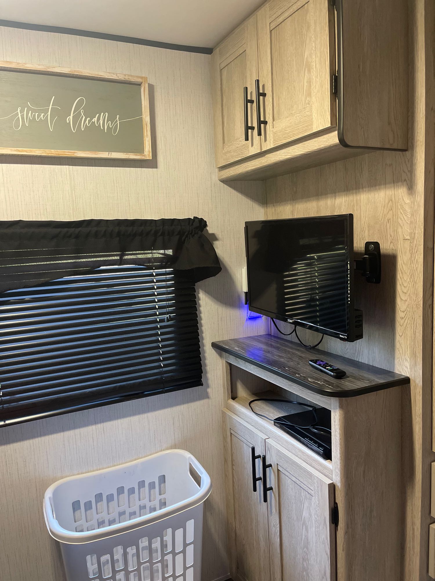 RV rental bedroom interior: Modern wood cabinets, mounted TV, window with blinds, and laundry basket for a cozy stay.. Heartland RVs Prowler 2022