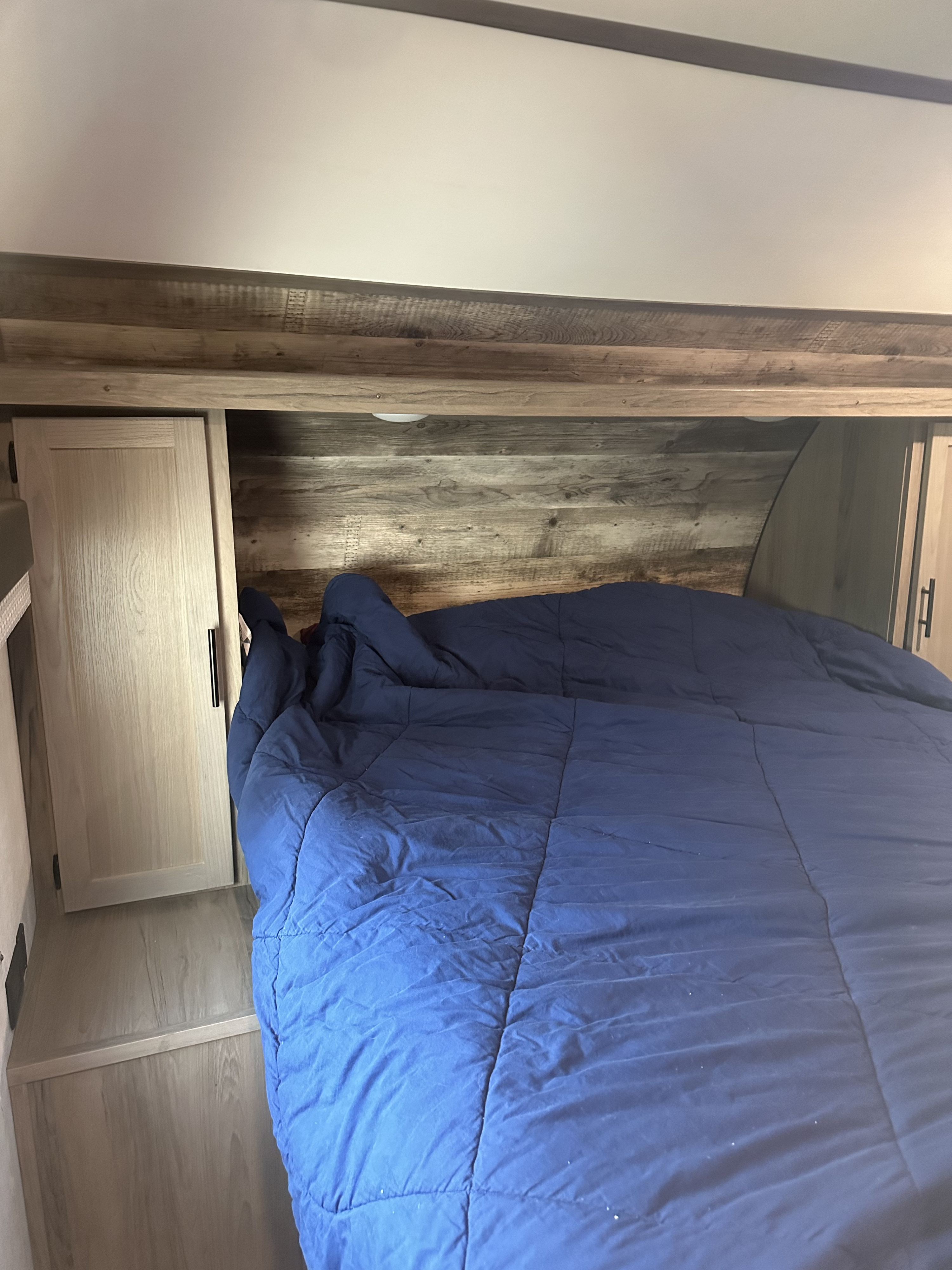 Cozy RV rental bedroom featuring a blue comforter, wood paneling, and built-in storage on both sides.. Gulf Stream Ameri-Lite 2022