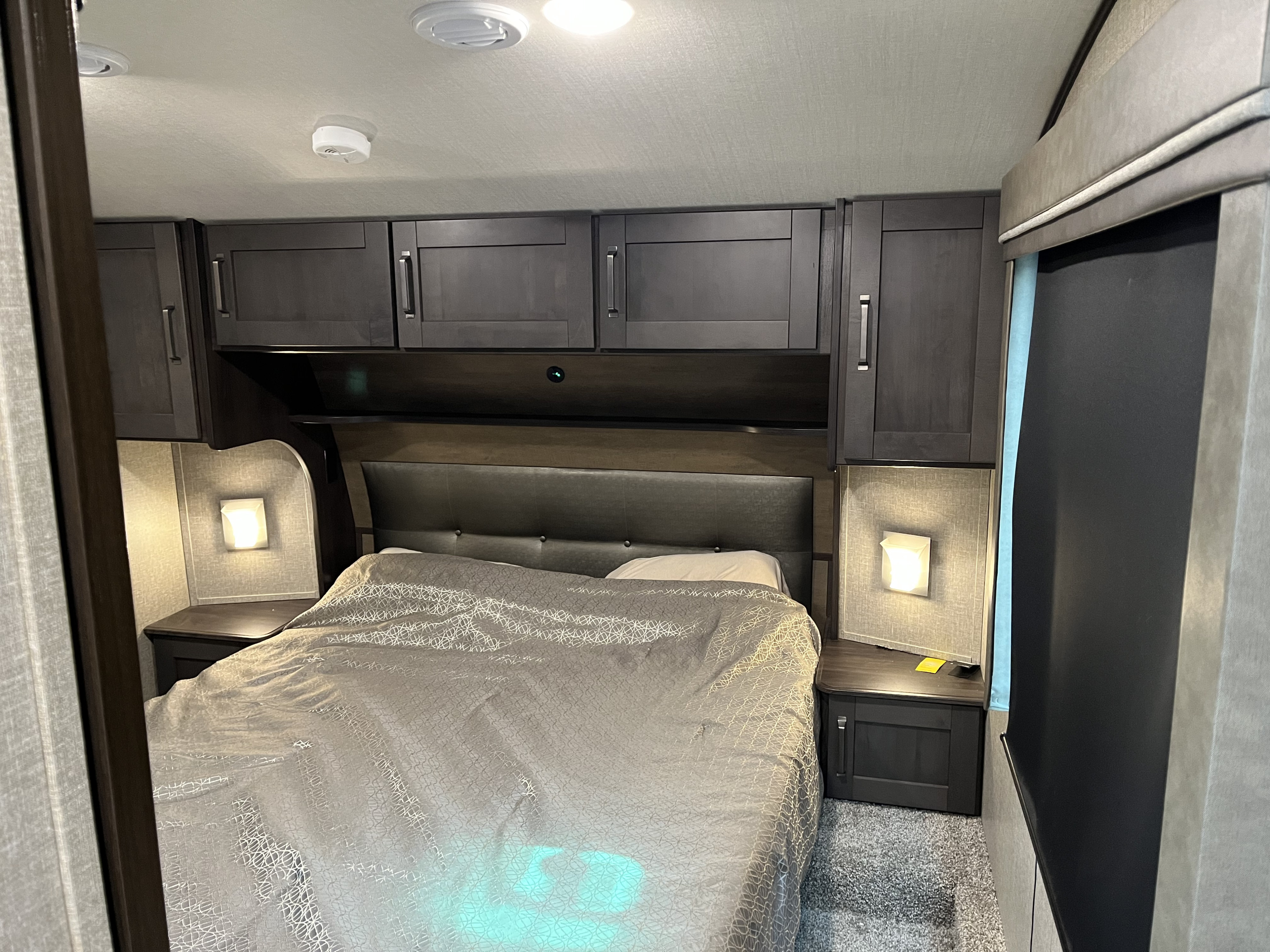 Cozy RV rental bedroom: bed with grey comforter, dark cabinets, and bedside lights, perfect for travel.. Grand Design Reflection 2022