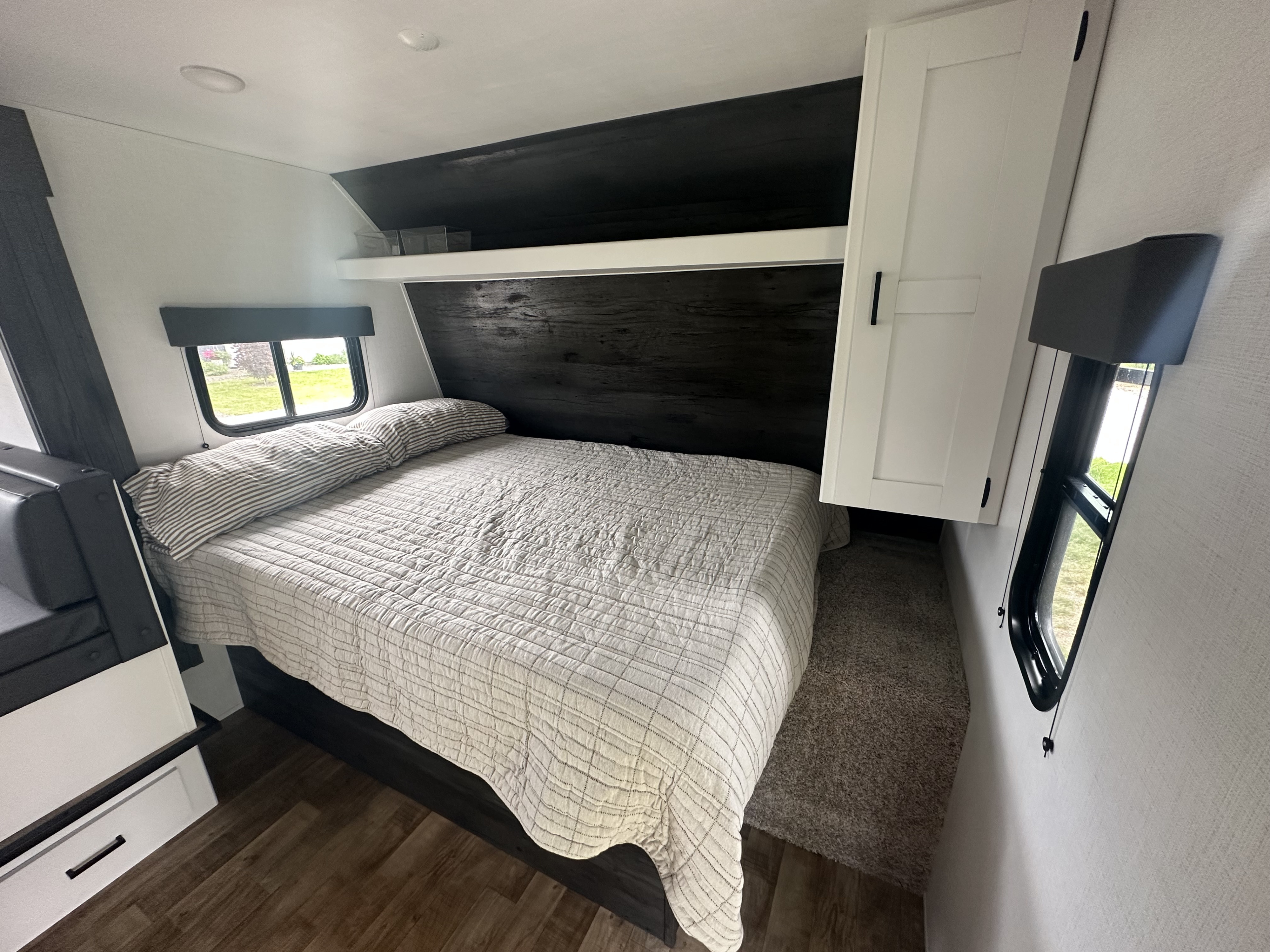 Inside your RV rental: a modern, compact bedroom with a cozy bed, striped pillow, dark wood headboard, and windows.. Keystone RV Hideout 2023