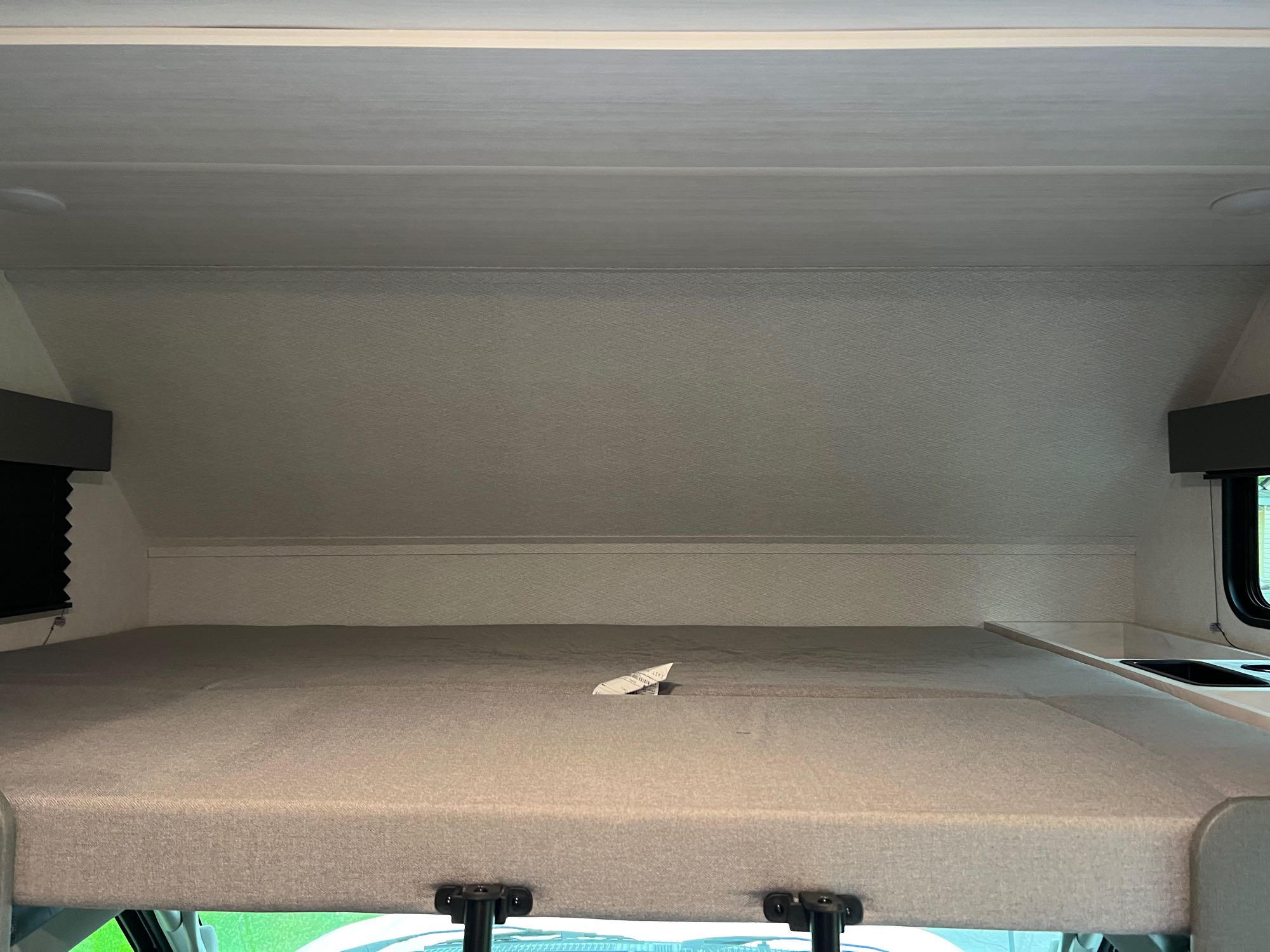 Spacious cab-over bunk bed in an RV rental, featuring a light grey mattress and a small sink area on the right.. EAST TO WEST ENTRADA 2600DS 2023