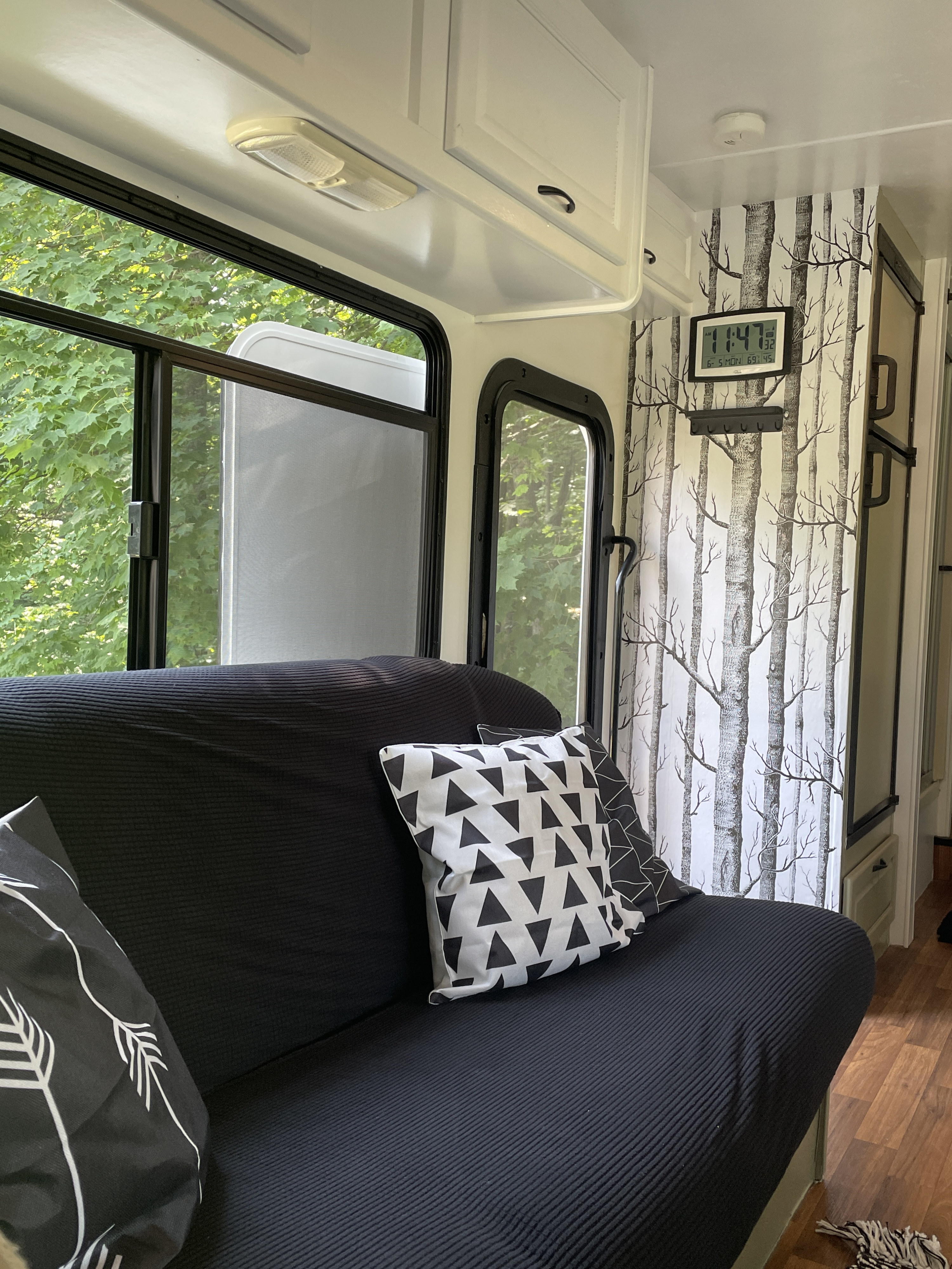 An inviting RV rental interior featuring a black sofa, patterned pillows, a birch tree accent wall, and a green window view.. Thor Majestic 2015