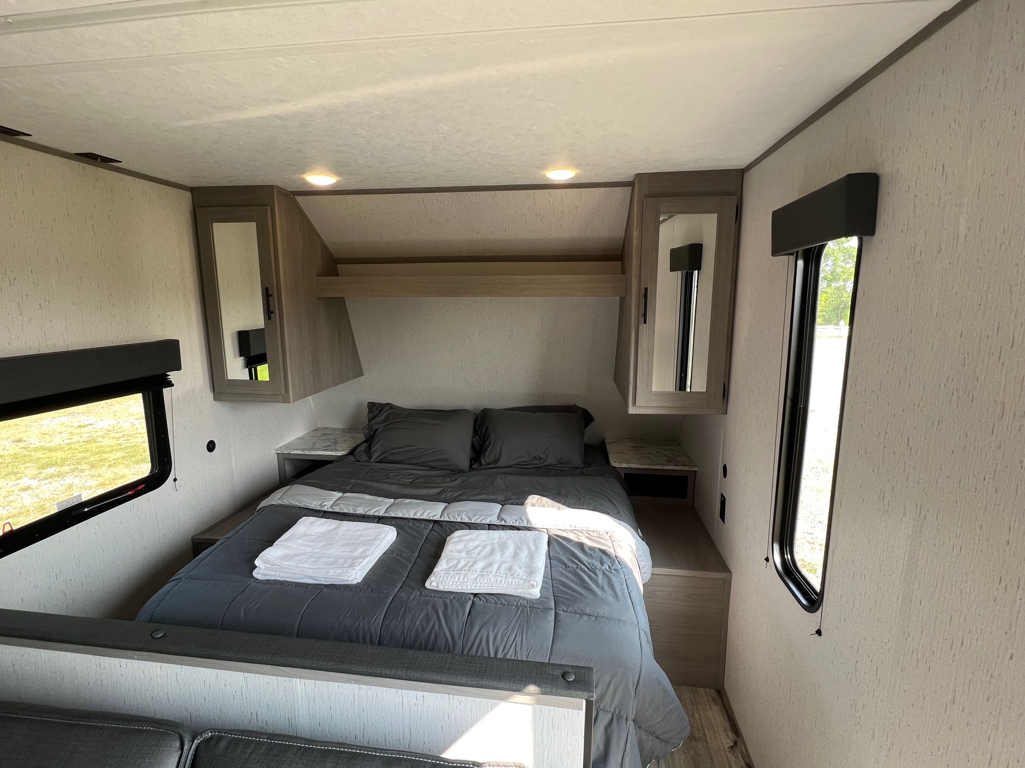 Step inside this cozy RV rental bedroom. Features a comfortable bed, mirrored cabinets, and windows with scenic views.. Dutchmen Coleman 2023