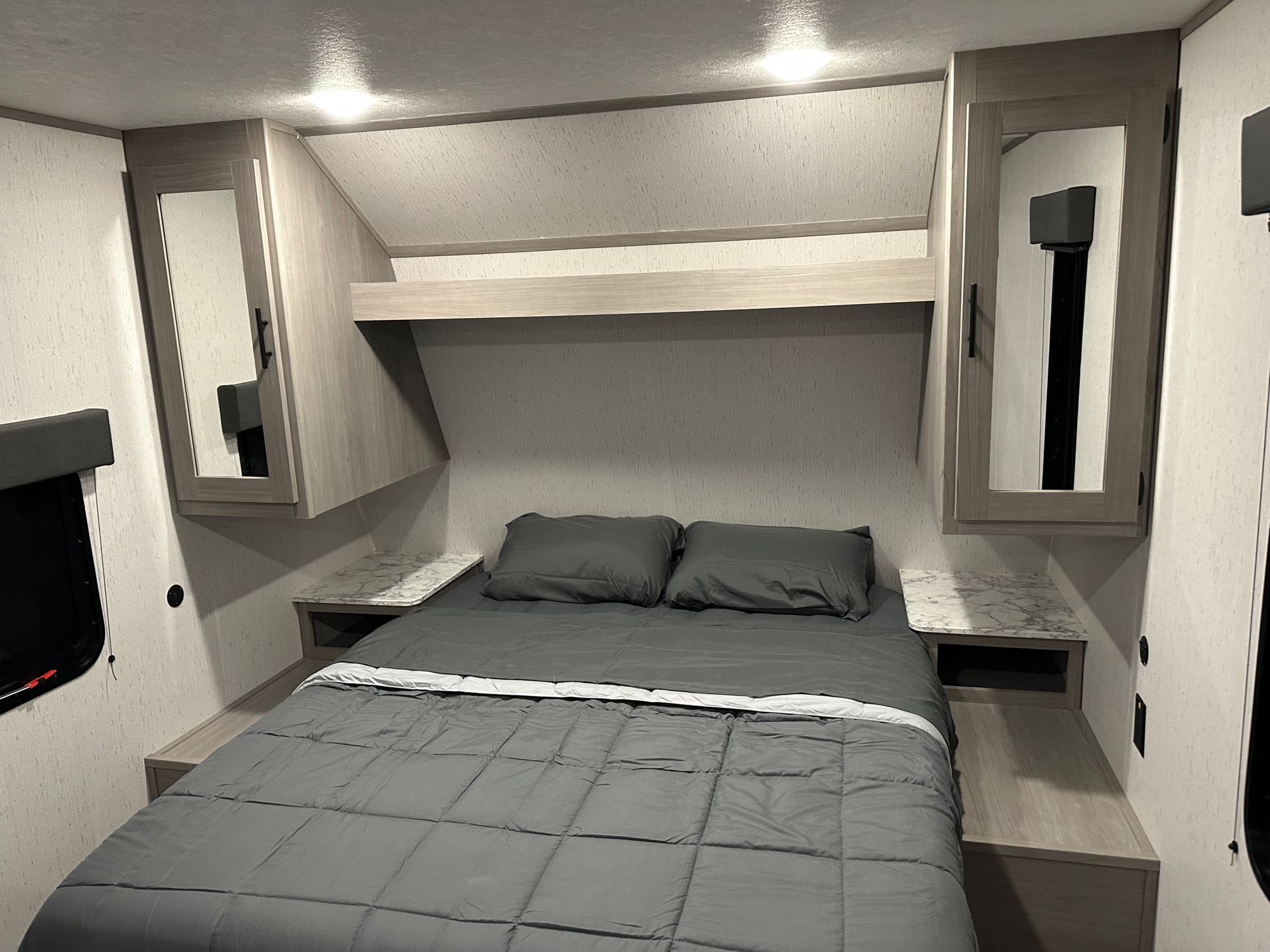 Clean RV rental bedroom: bed with grey linens, mirror-fronted cabinets, and floating nightstands. Ready for adventure!. Dutchmen Coleman 2023