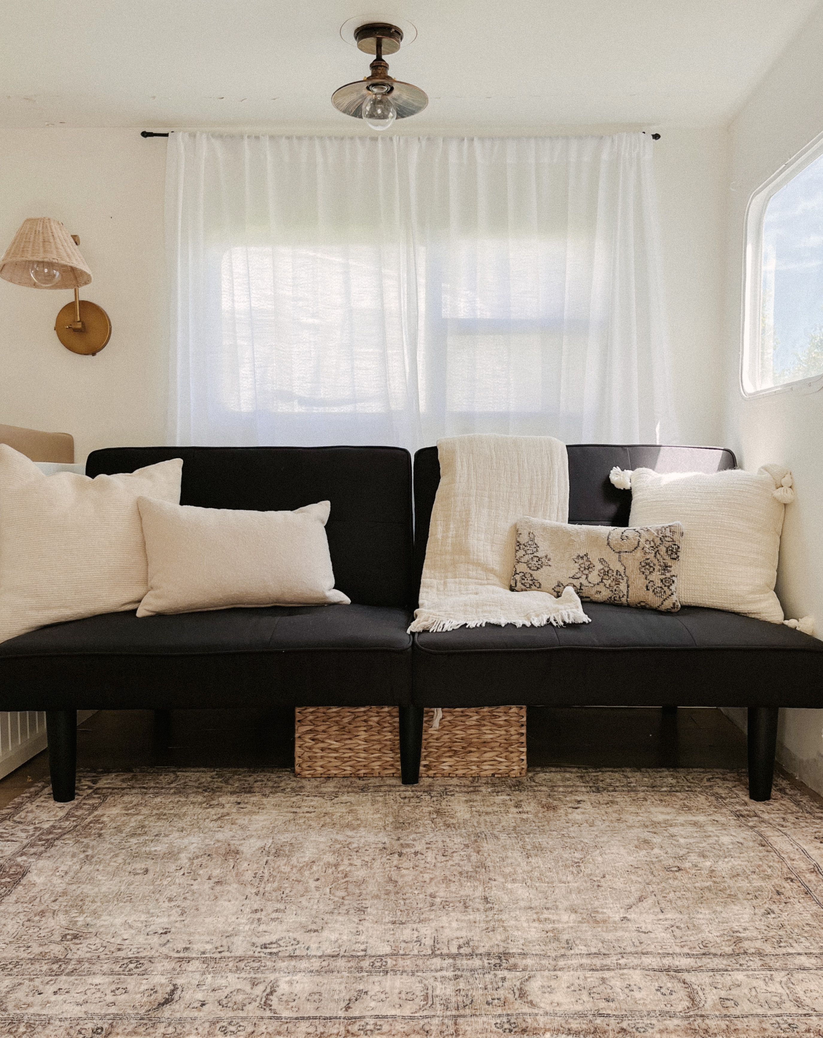 Inside a stylish RV rental: a black futon, neutral pillows & throw, patterned rug, and bright, curtained windows.. Wilderness Wilderness Trailer 2001