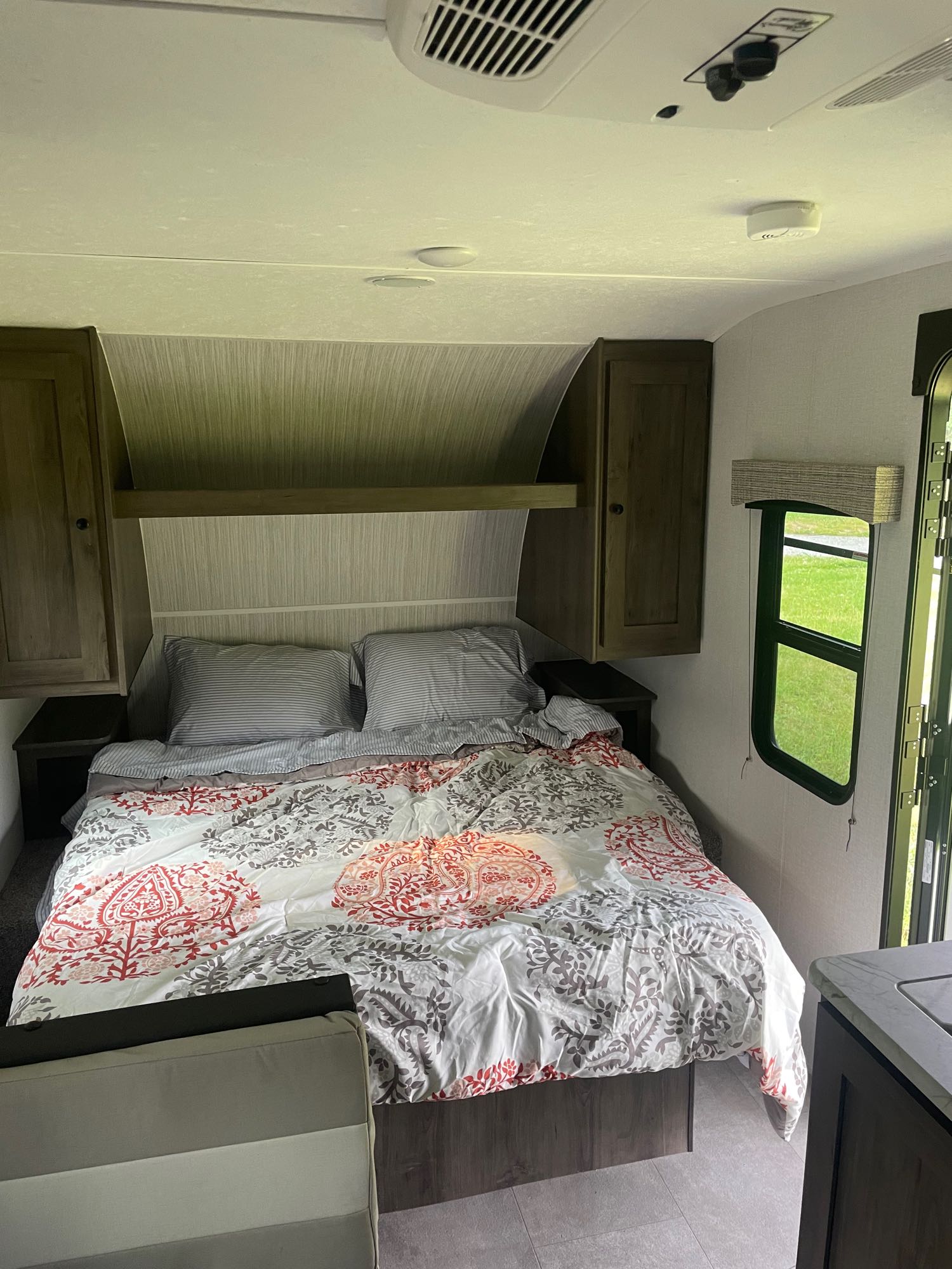 Cozy RV rental bedroom featuring a bed with patterned bedding, overhead cabinets, AC, and a window.. Forest River independence Trail 2022