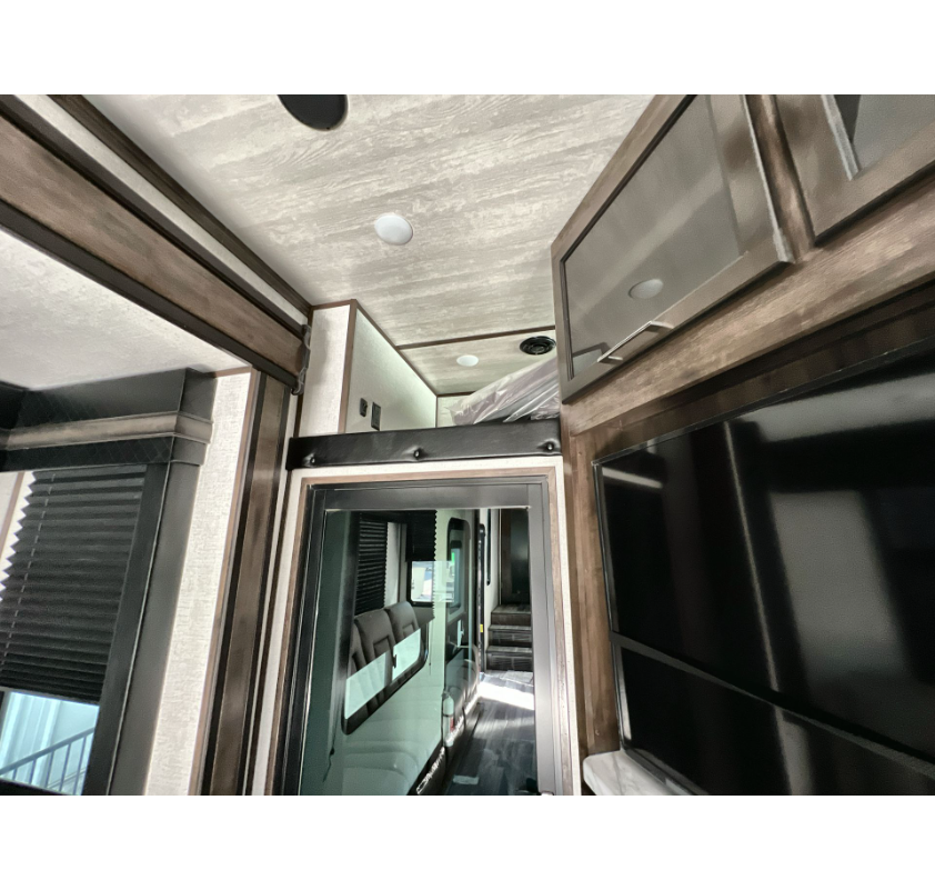 Inside a modern RV rental: view of living space with TV, sleek cabinetry, and a cozy overhead sleeping loft.. Dutchmen Voltage 2022