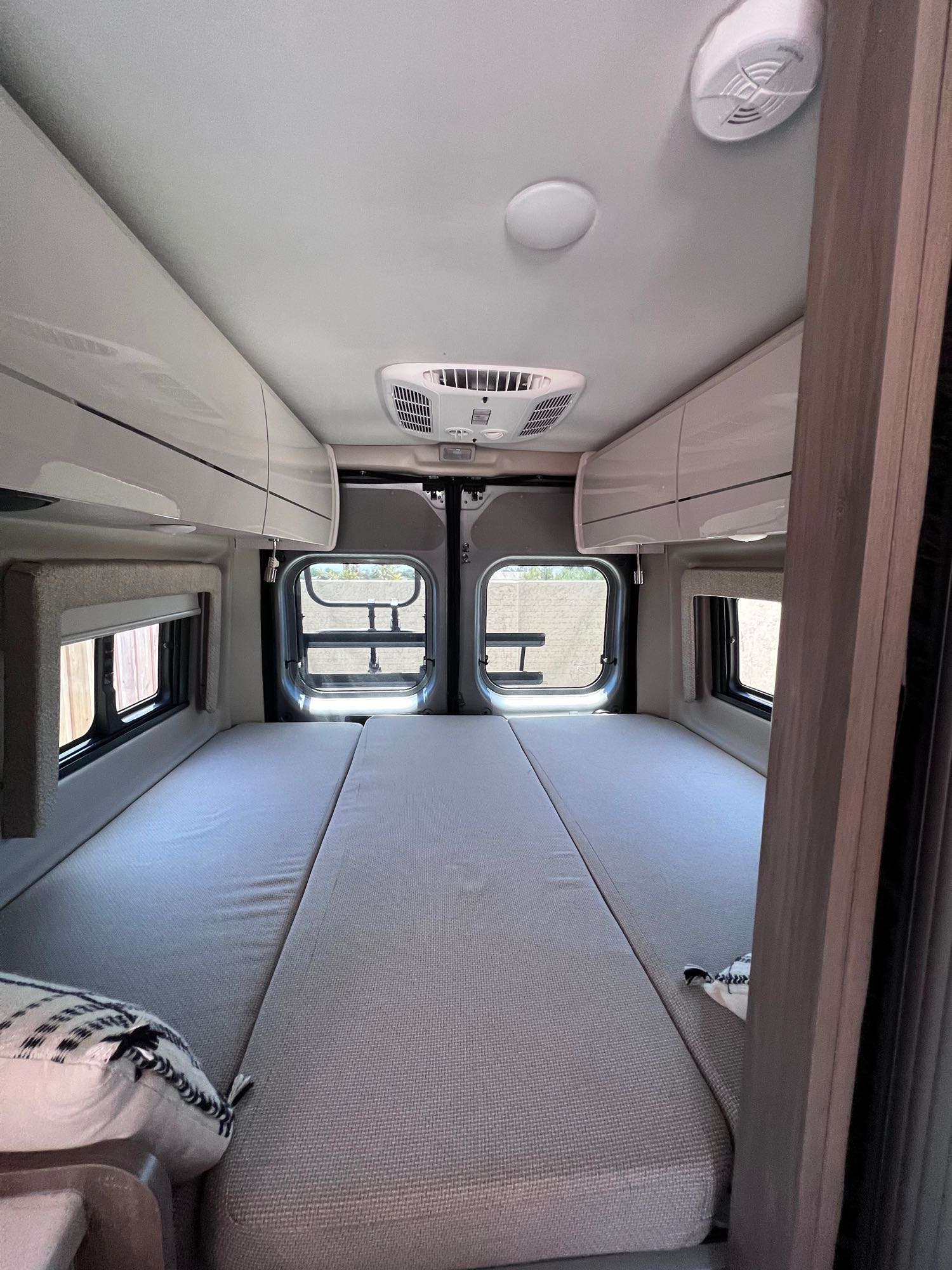 Spacious RV rental interior featuring a large bed, overhead storage, AC unit, and rear windows, ready for travel.. Thor Tellaro 2021
