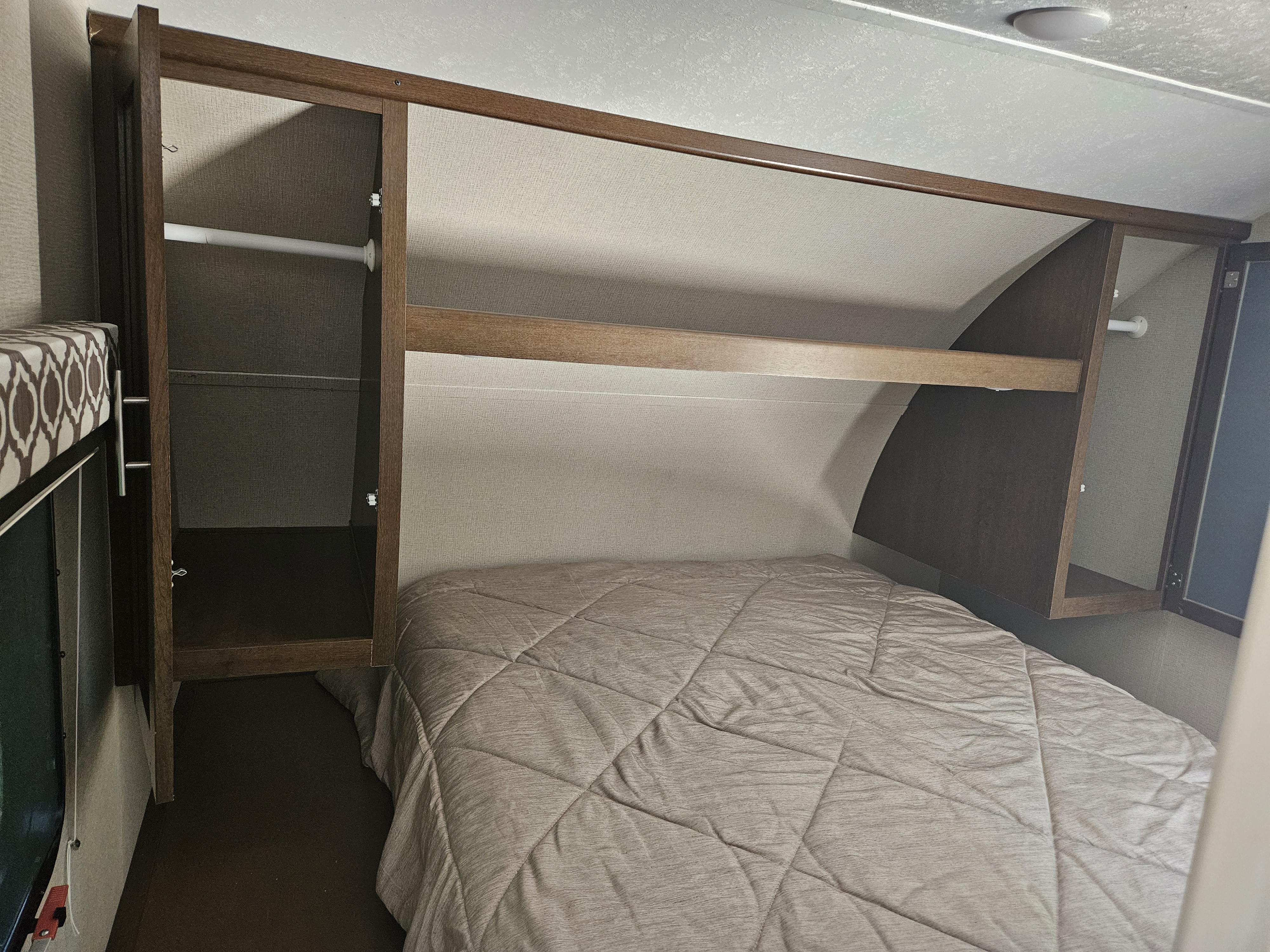 RV rental bedroom setup with a comfortable bed, overhead shelf, and wardrobe space, ready for travel.. Forest River Tracer Breeze 2019