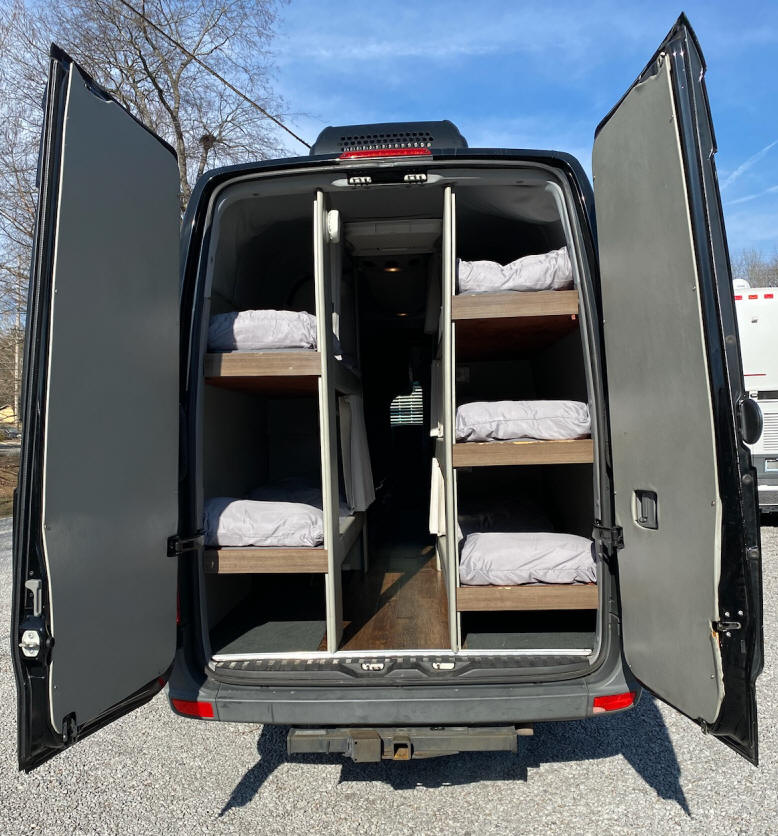 RV rental: Back of a black camper van with open doors reveals six bunk beds inside for mobile sleeping.. Mercedes-Benz Sprinter 2012