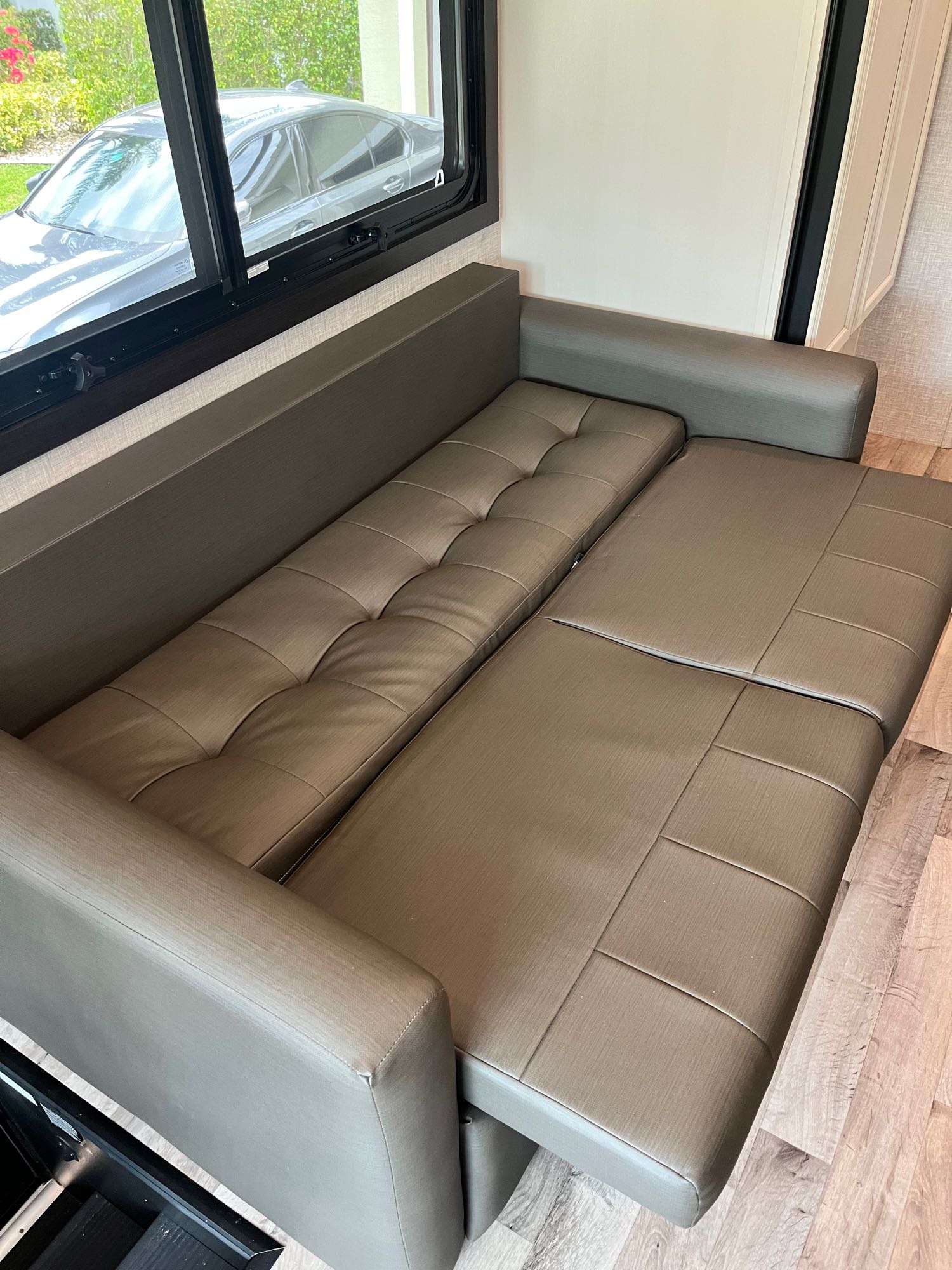 Spacious RV rental interior with a brown convertible sleeper sofa extended for use. A car is visible through the window.. Entegra Vision 2023