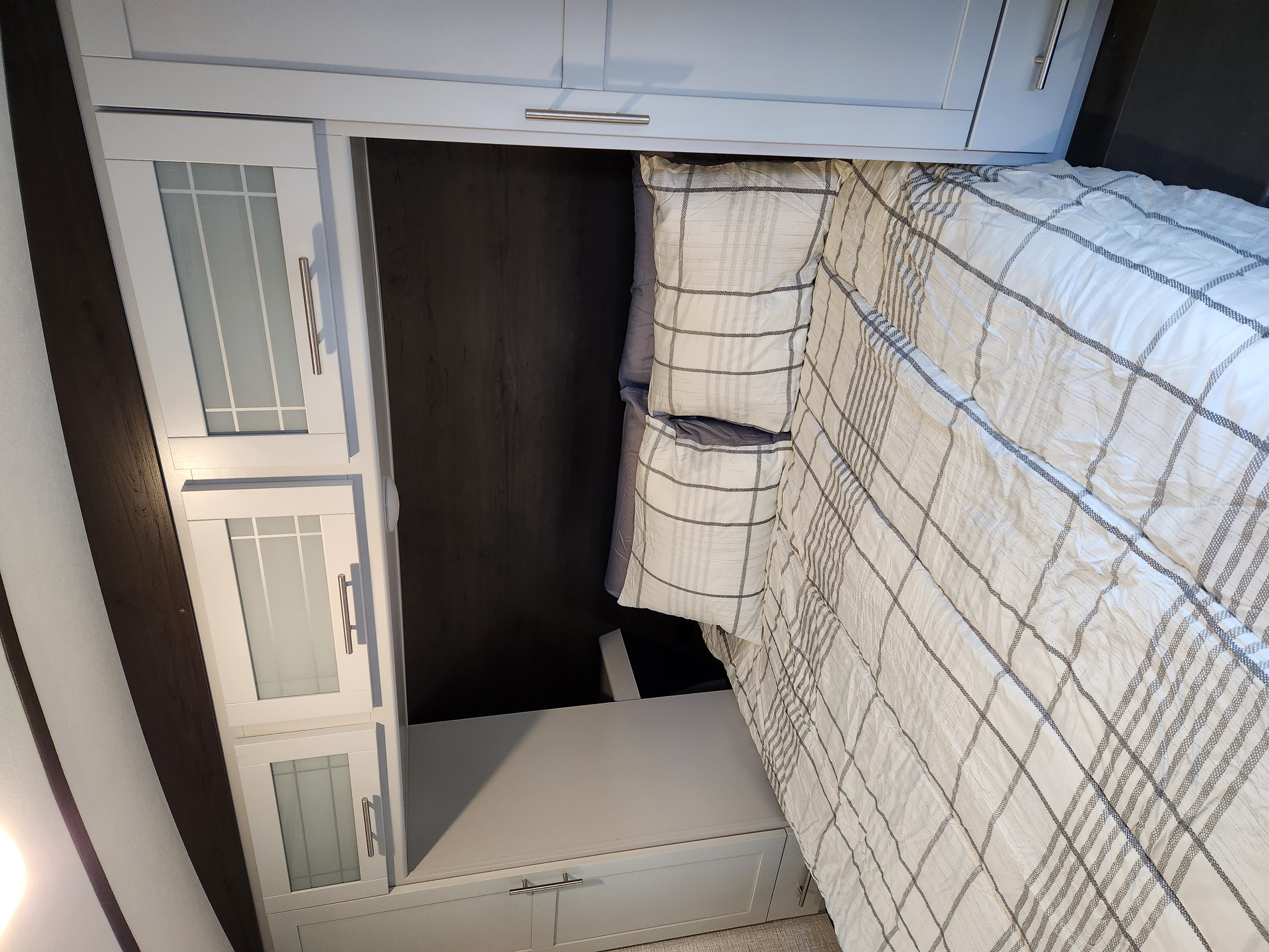Functional RV rental bedroom with modern light grey cabinets, under-bed storage, and crisp white plaid bedding.. Keystone RV Bullet Ultra Lite 2021