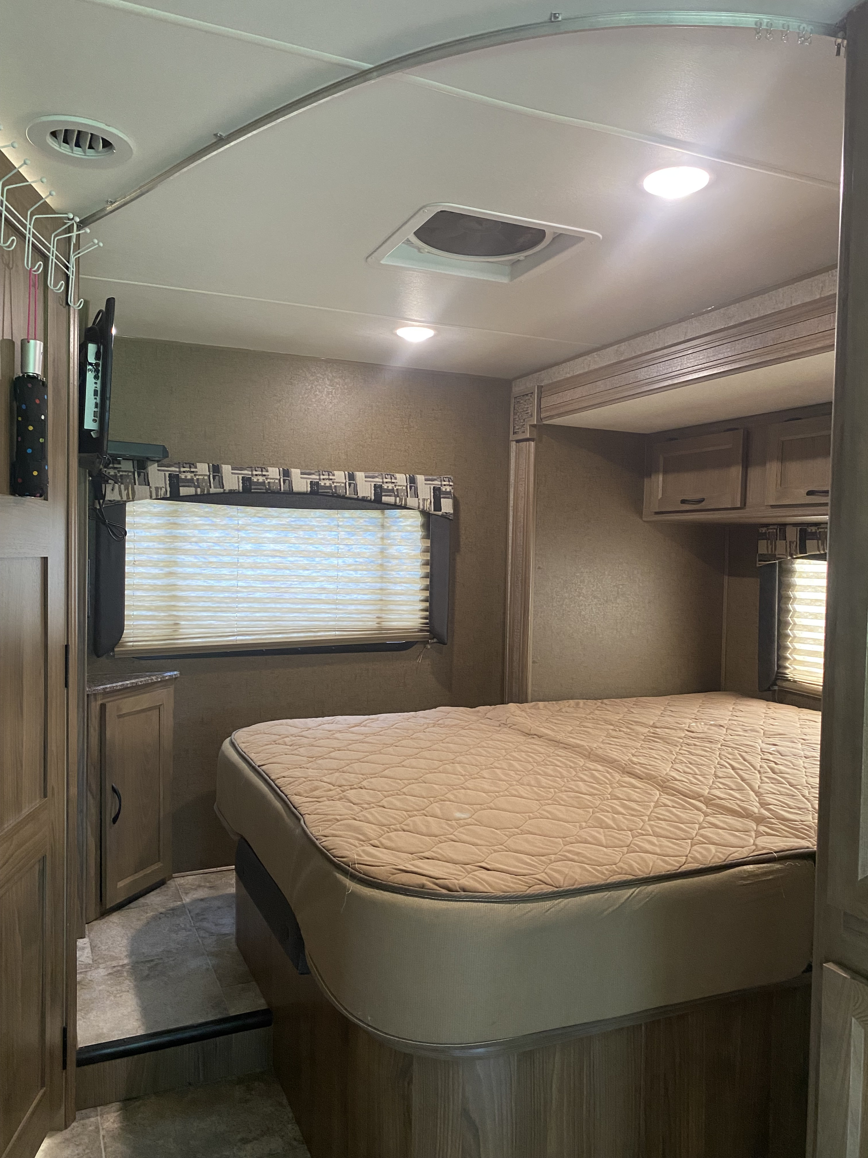 Bedroom view in an RV rental, featuring a quilted bed, overhead cabinets, window blinds, and coat hooks. Ideal for travel.. Coachmen Freelander 26 RS 2017