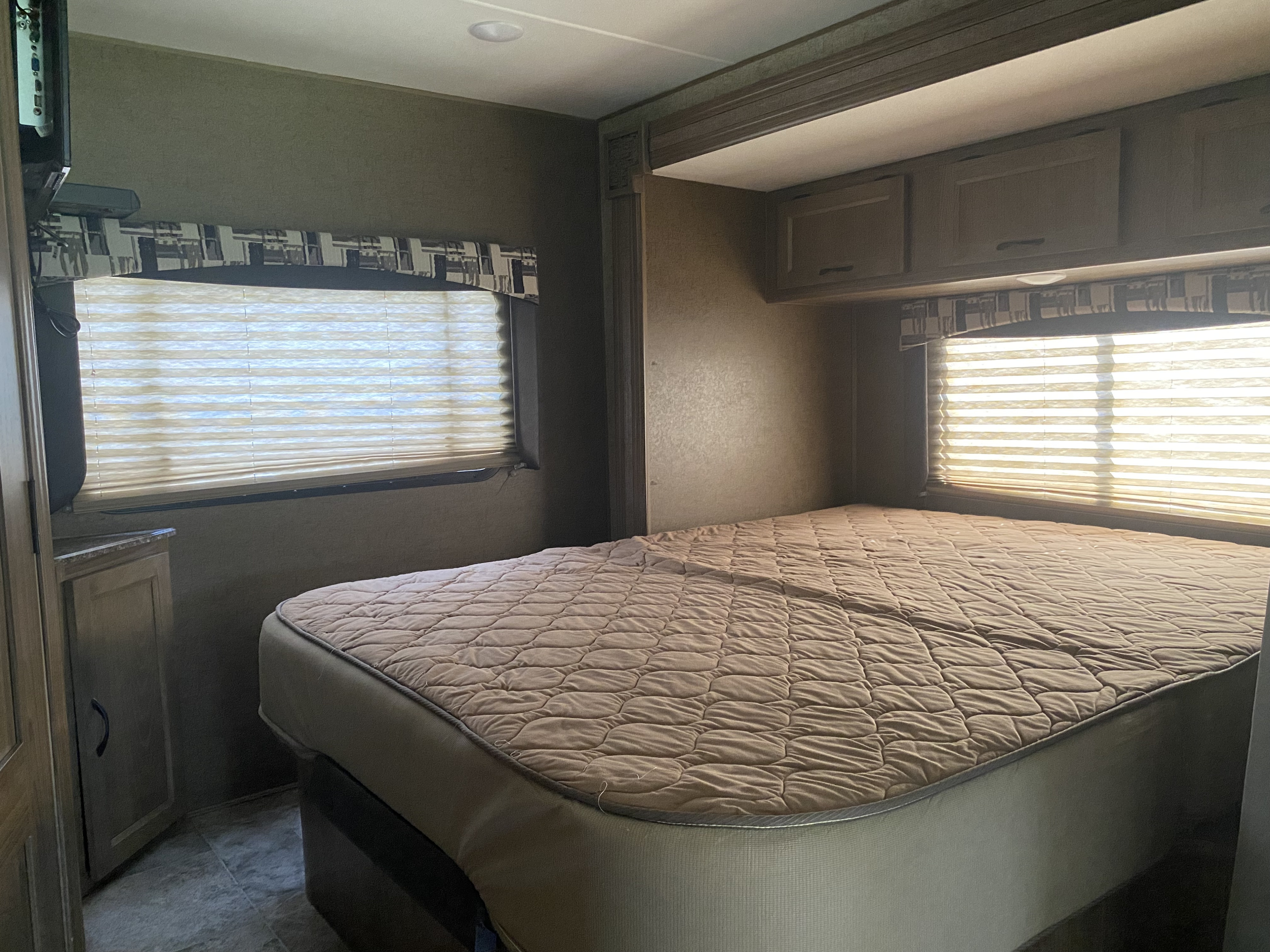 Cozy bedroom in an RV rental, featuring a large bed with a quilted cover, windows with blinds, and overhead cabinets.. Coachmen Freelander 26 RS 2017