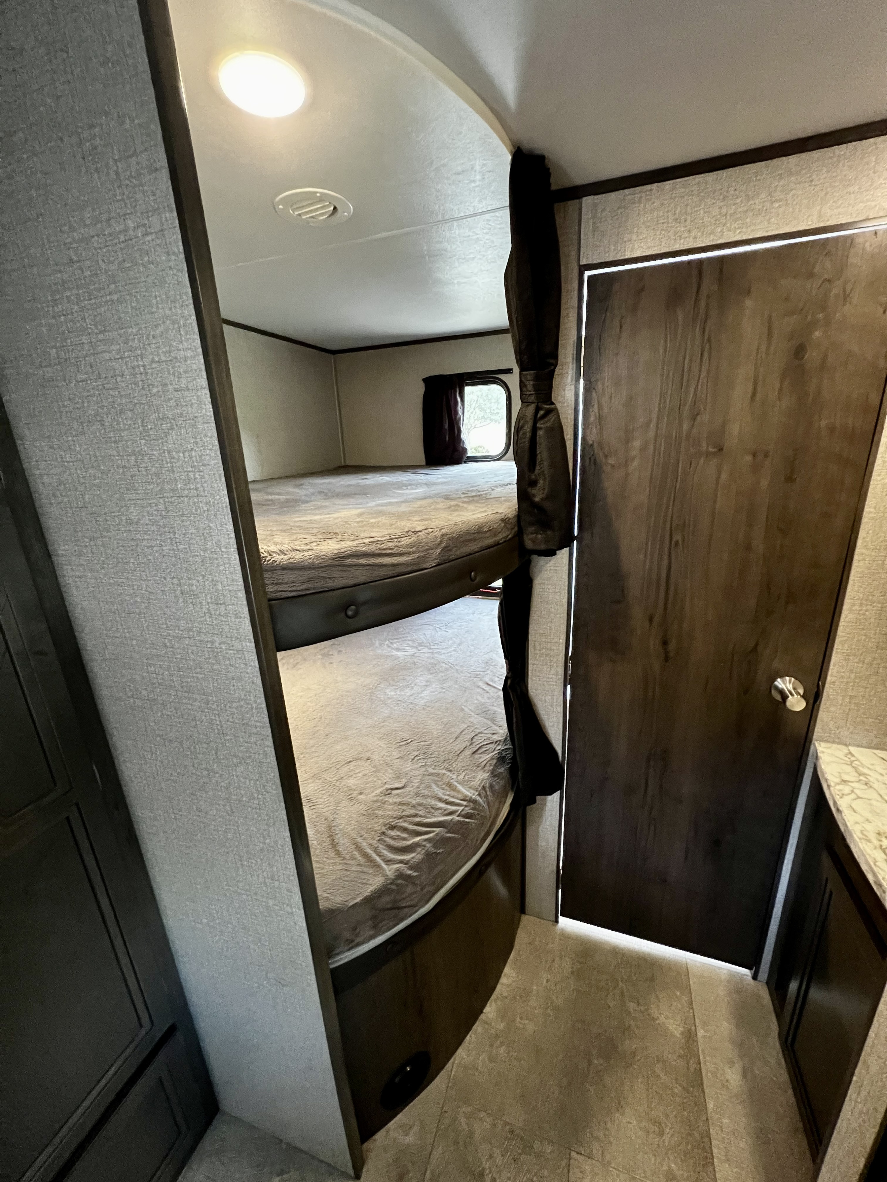 RV rental interior: cozy bunk beds with light gray bedding, a window, and dark wood door.. Jayco Jay Flight SLX 2020