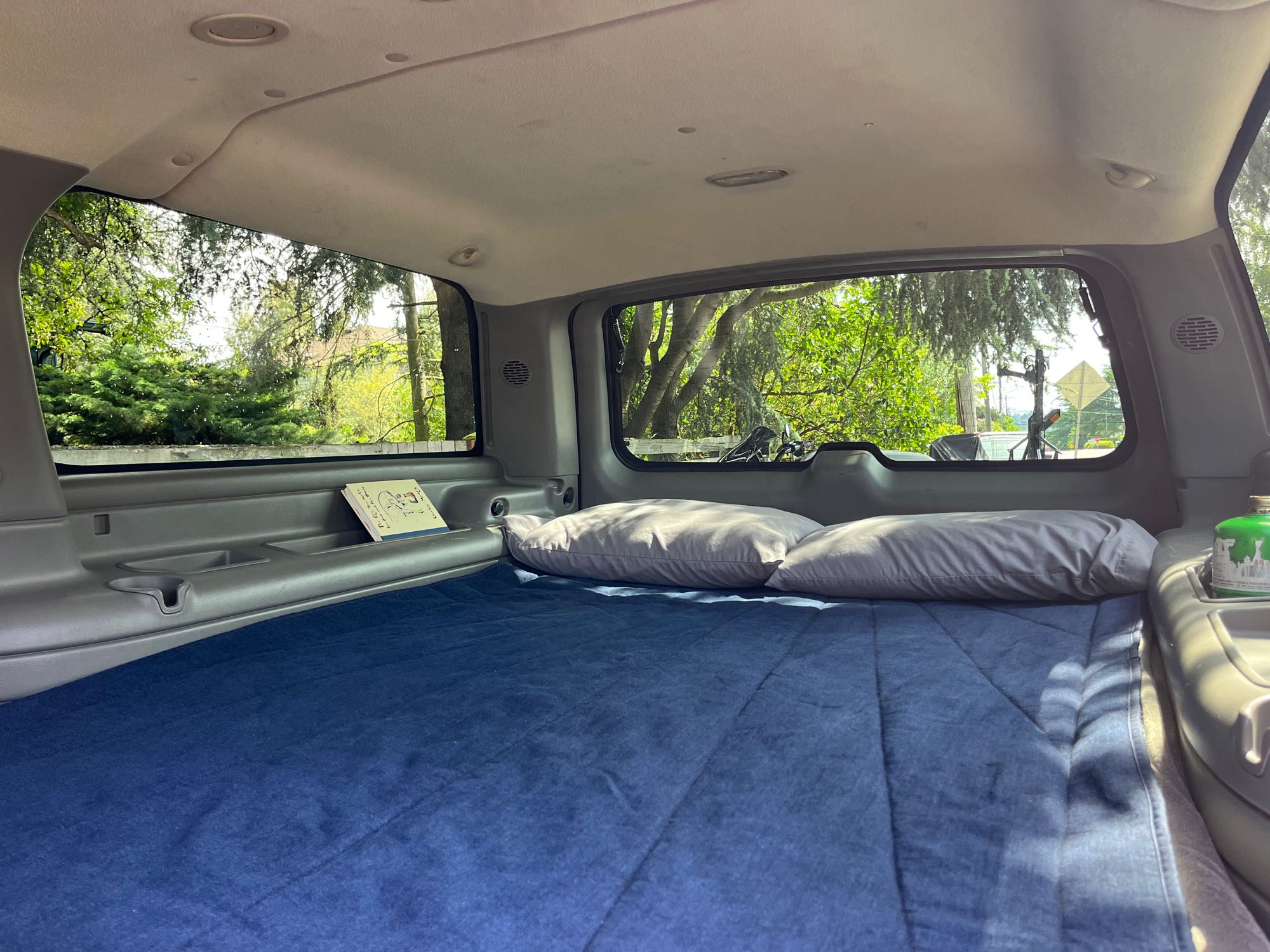 Interior of a vehicle transformed into a cozy bed space for road trips, ideal for an RV rental alternative. Complete with pillows & views.. Gmc Yukon XL 2005