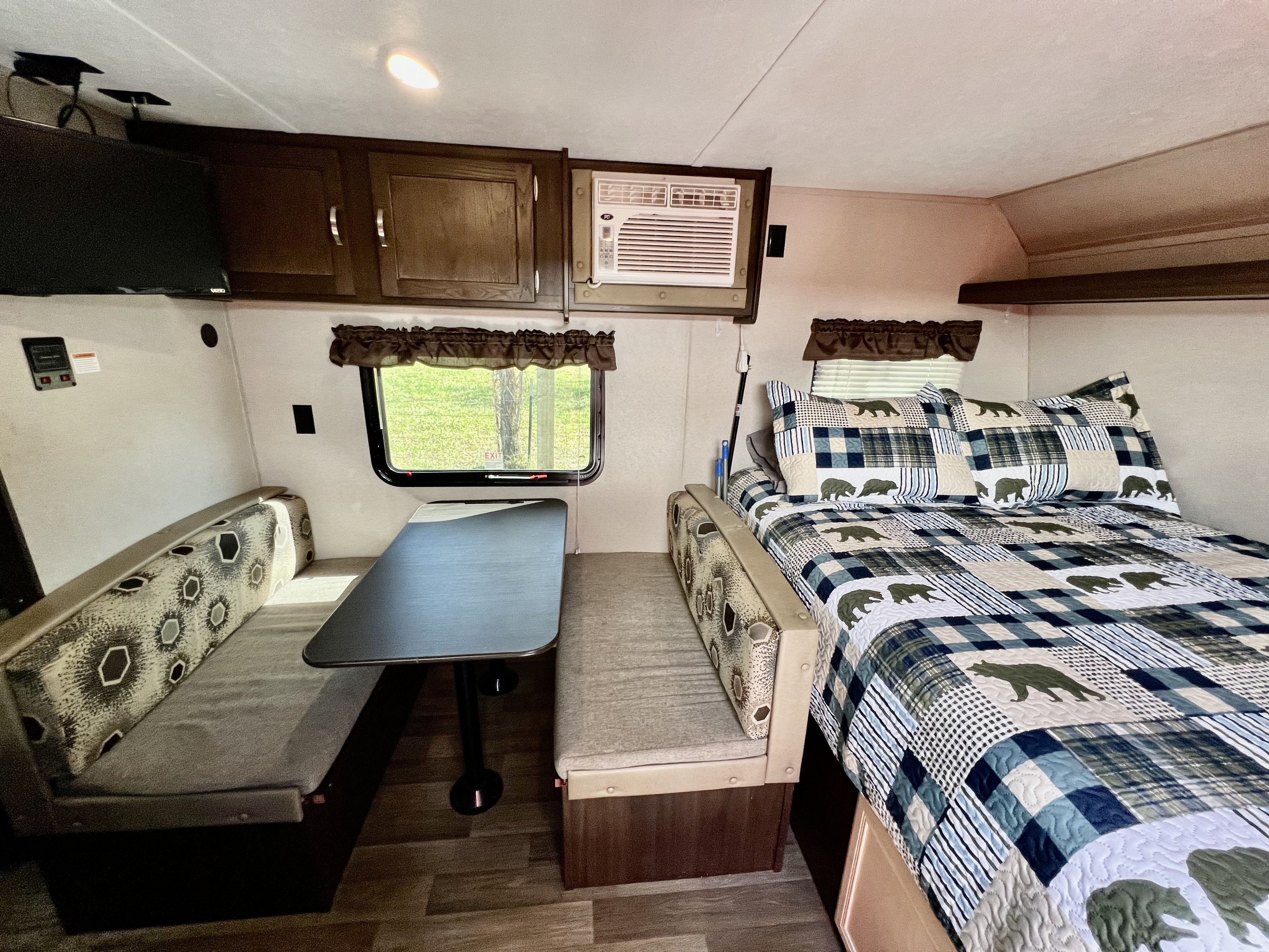 This RV rental interior features a cozy bed with a bear quilt, a practical dinette, and overhead cabinets.. Keystone RV Springdale Mini 1800BH 2018
