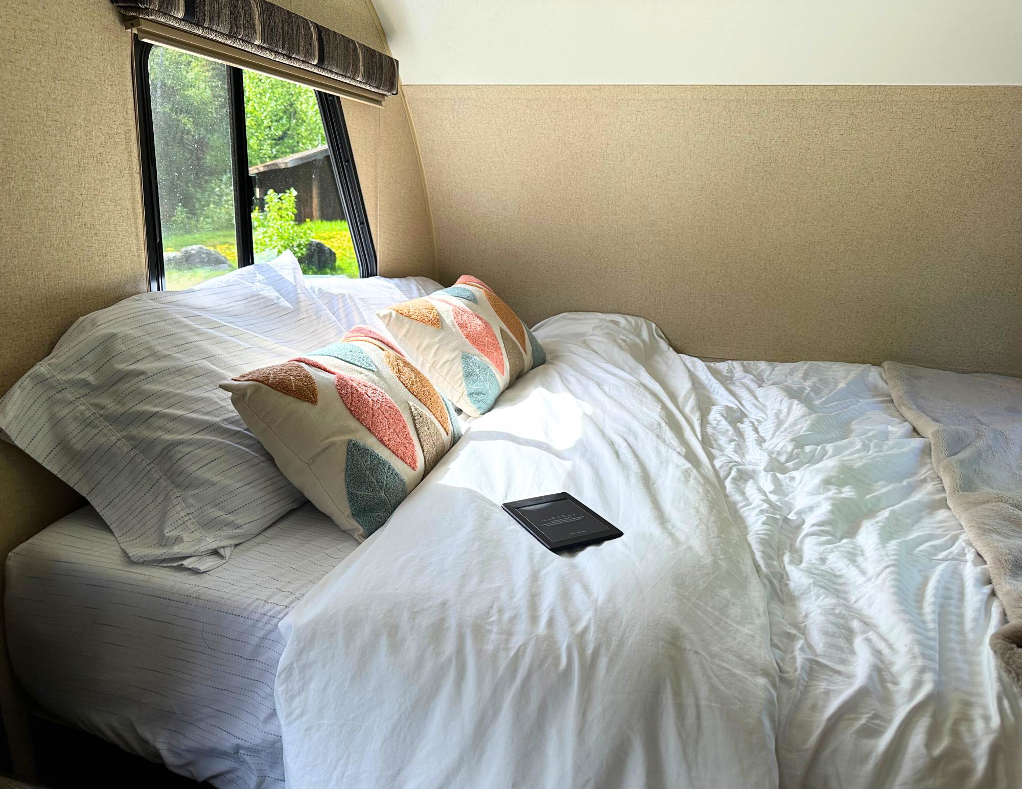 Bright RV rental bedroom featuring a comfy bed, colorful pillows, e-reader, and a nature view from the window.. R-Pod Hood River Edition 2015
