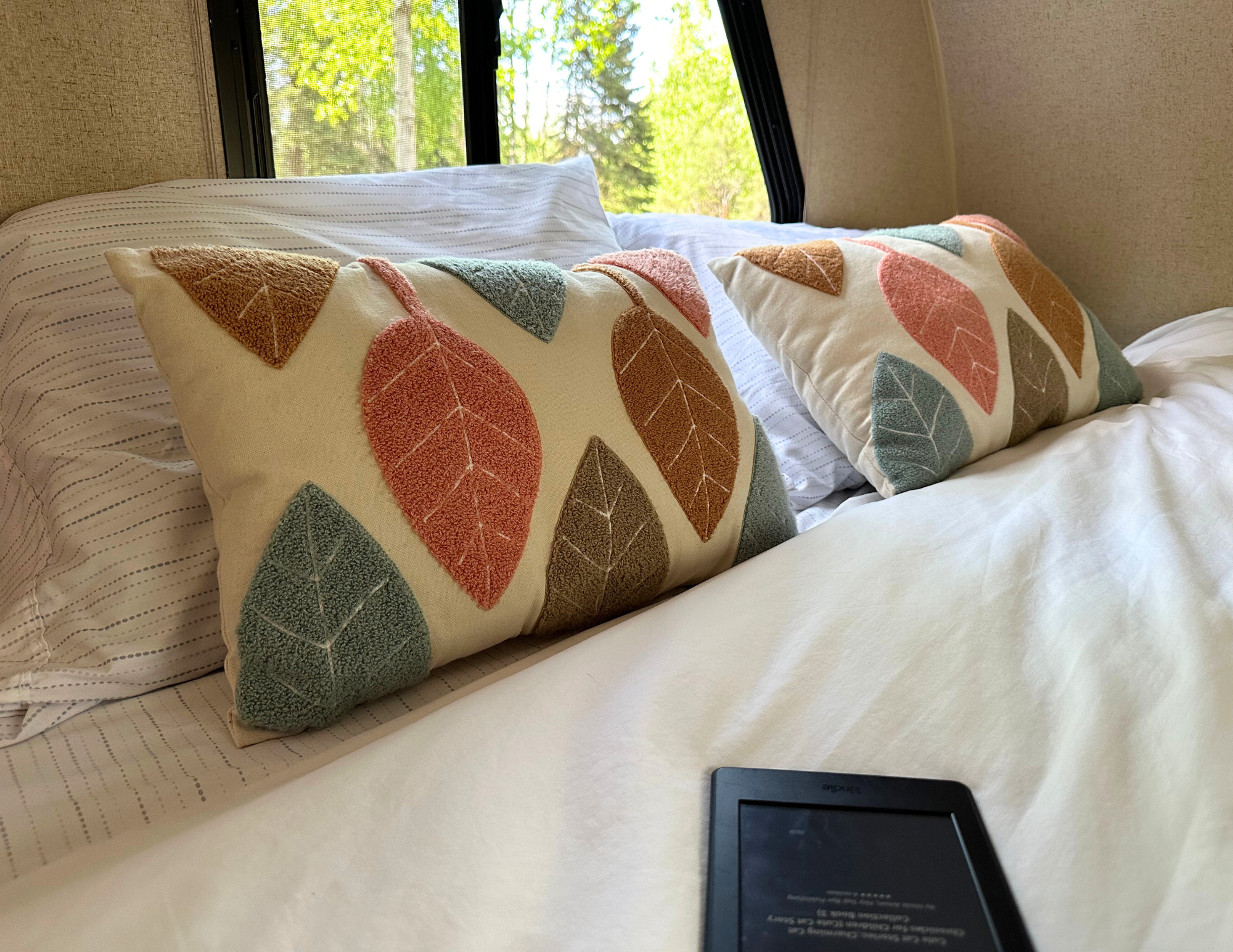 A cozy bed in an RV rental, adorned with colorful leaf pillows and a Kindle, offering a peaceful retreat.. R-Pod Hood River Edition 2015