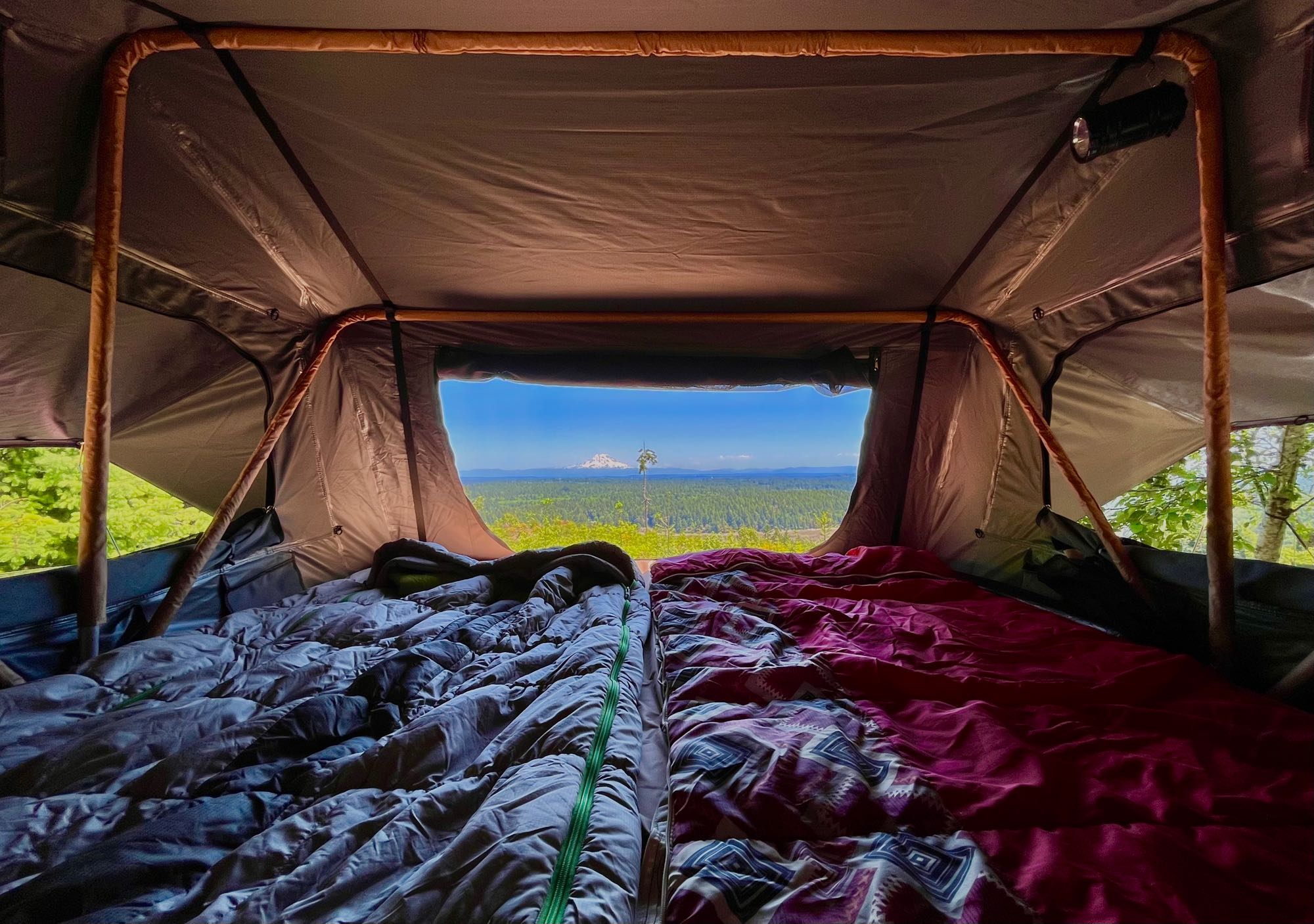 Inside a spacious rooftop tent with two cozy beds, offering a stunning view of a distant mountain and forest; ideal for RV rental trips.. Gmc Yukon XL 2005