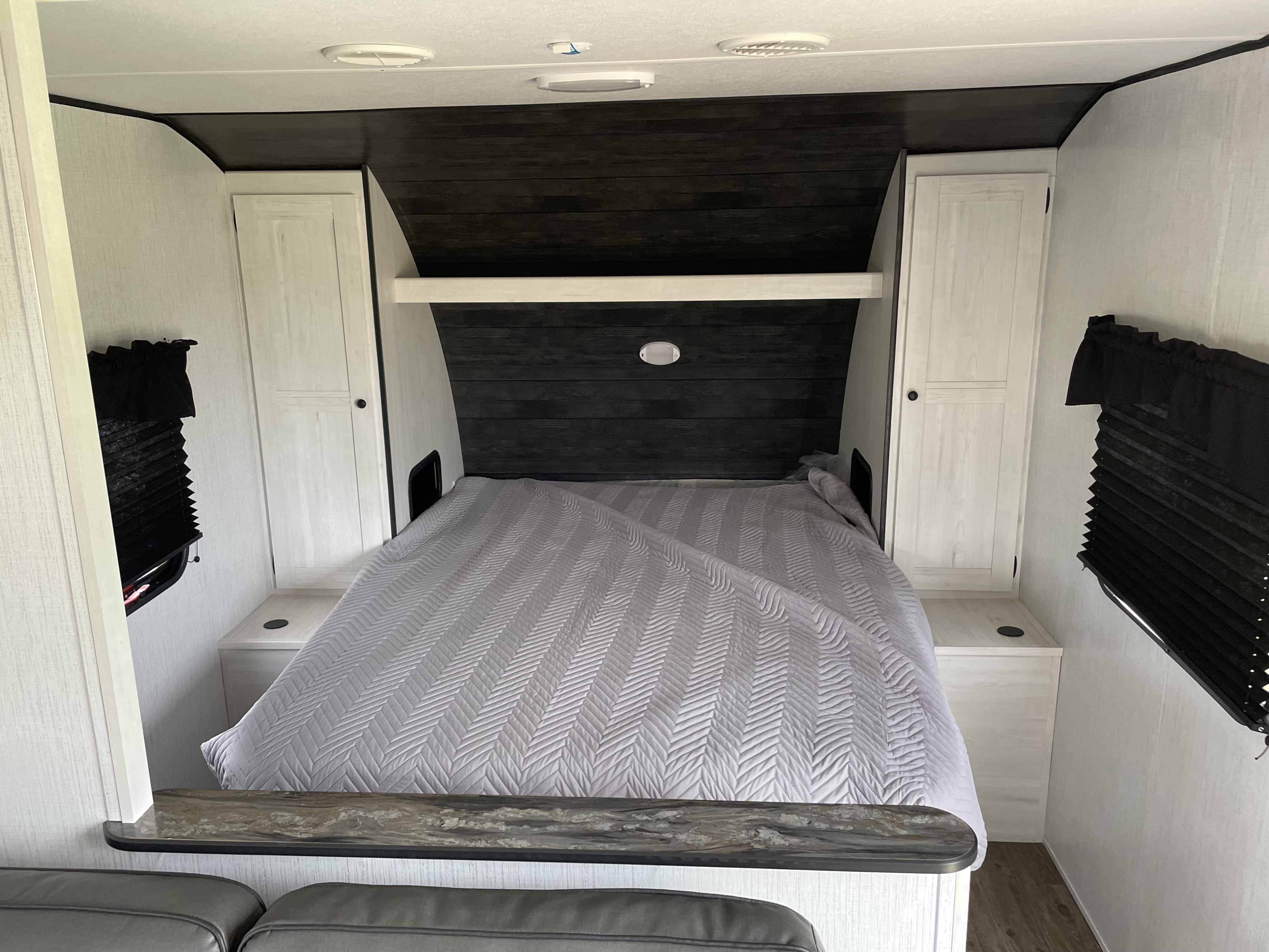 An RV rental's cozy bedroom, featuring a gray quilted bed, white built-in cabinets, and dark headboard details.. Heartland RVs Trail Runner 2022