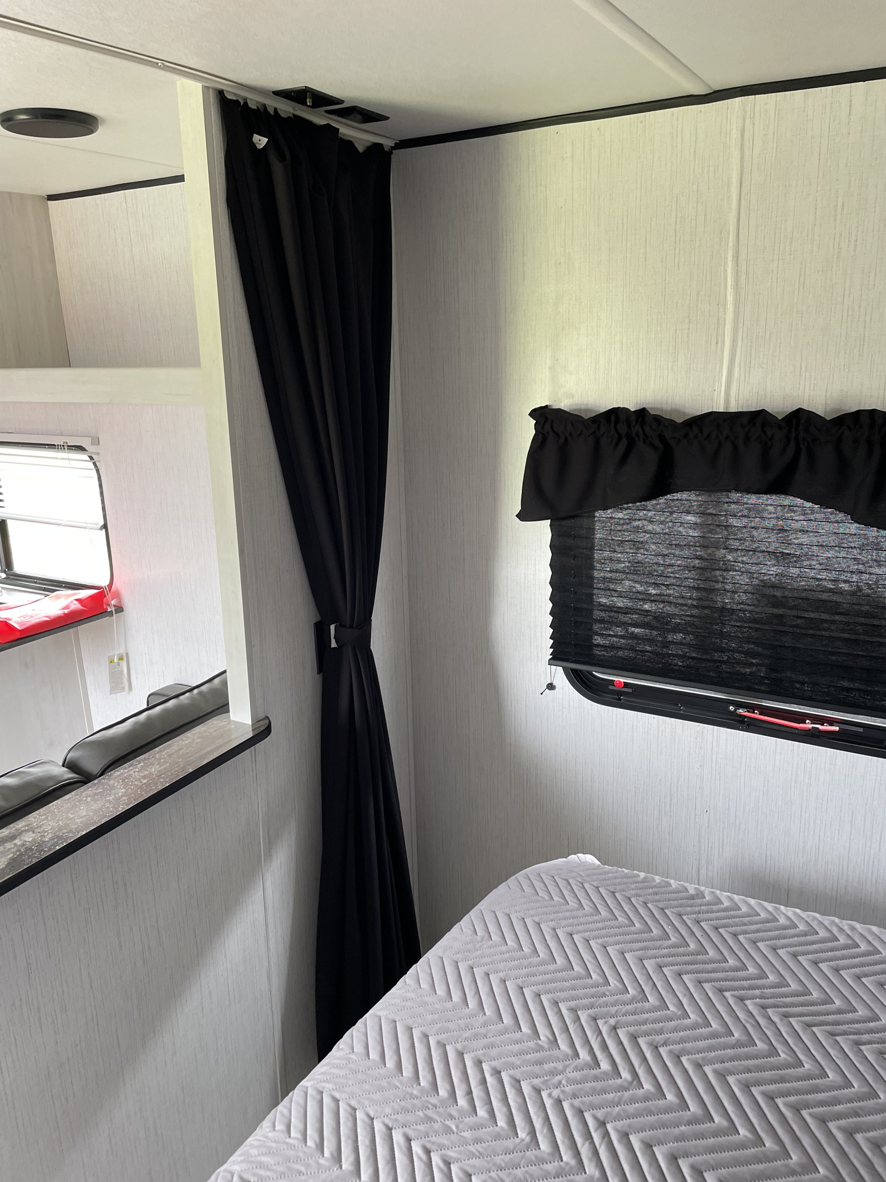 RV rental interior bedroom view with blackout curtains tied back, a window blind, and a quilted bed. Another section is visible.. Heartland RVs Trail Runner 2022