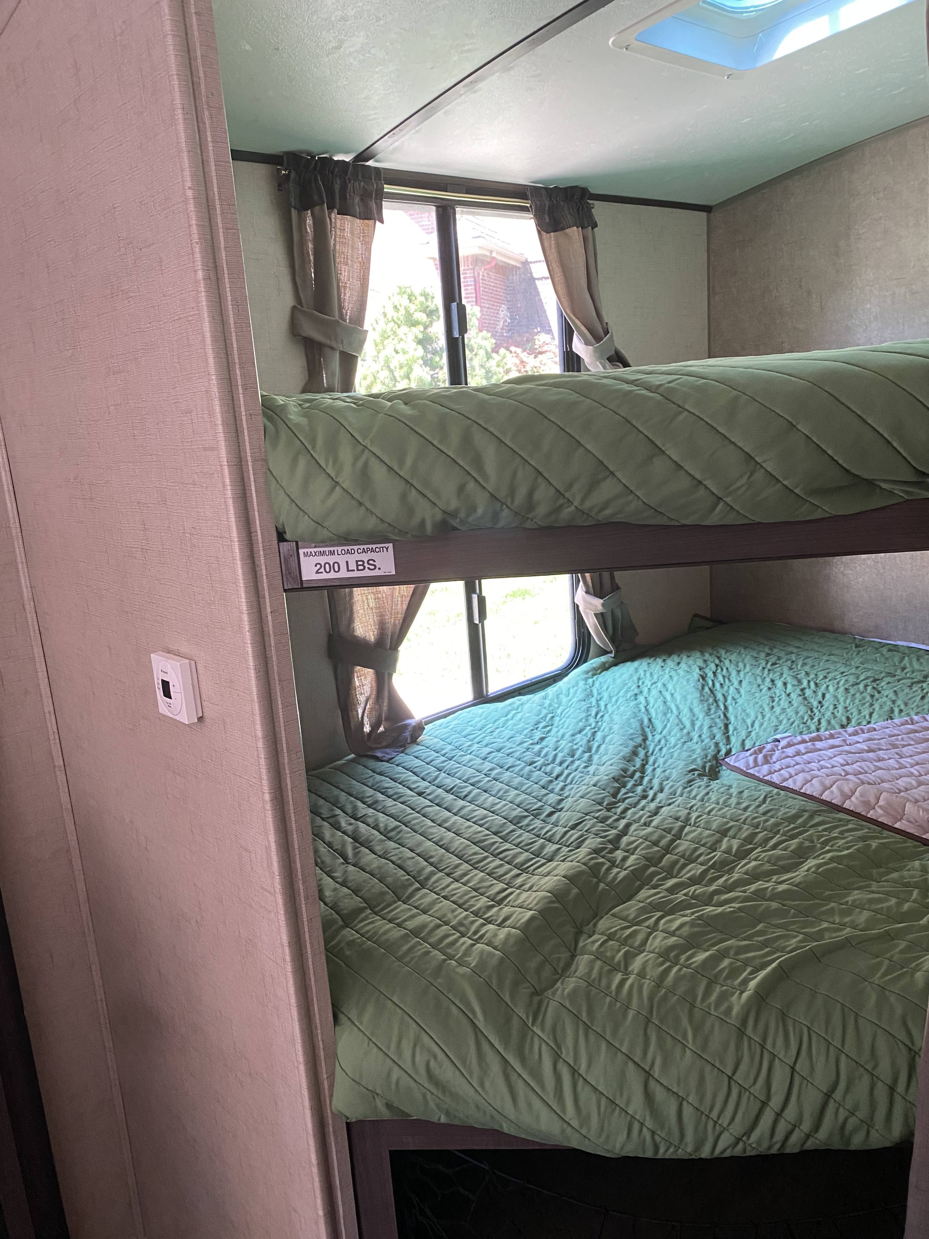 Interior of an RV rental: two cozy bunk beds with green quilted bedding and windows. Top bunk capacity is 200 lbs.. Forest River Surveyor 2017