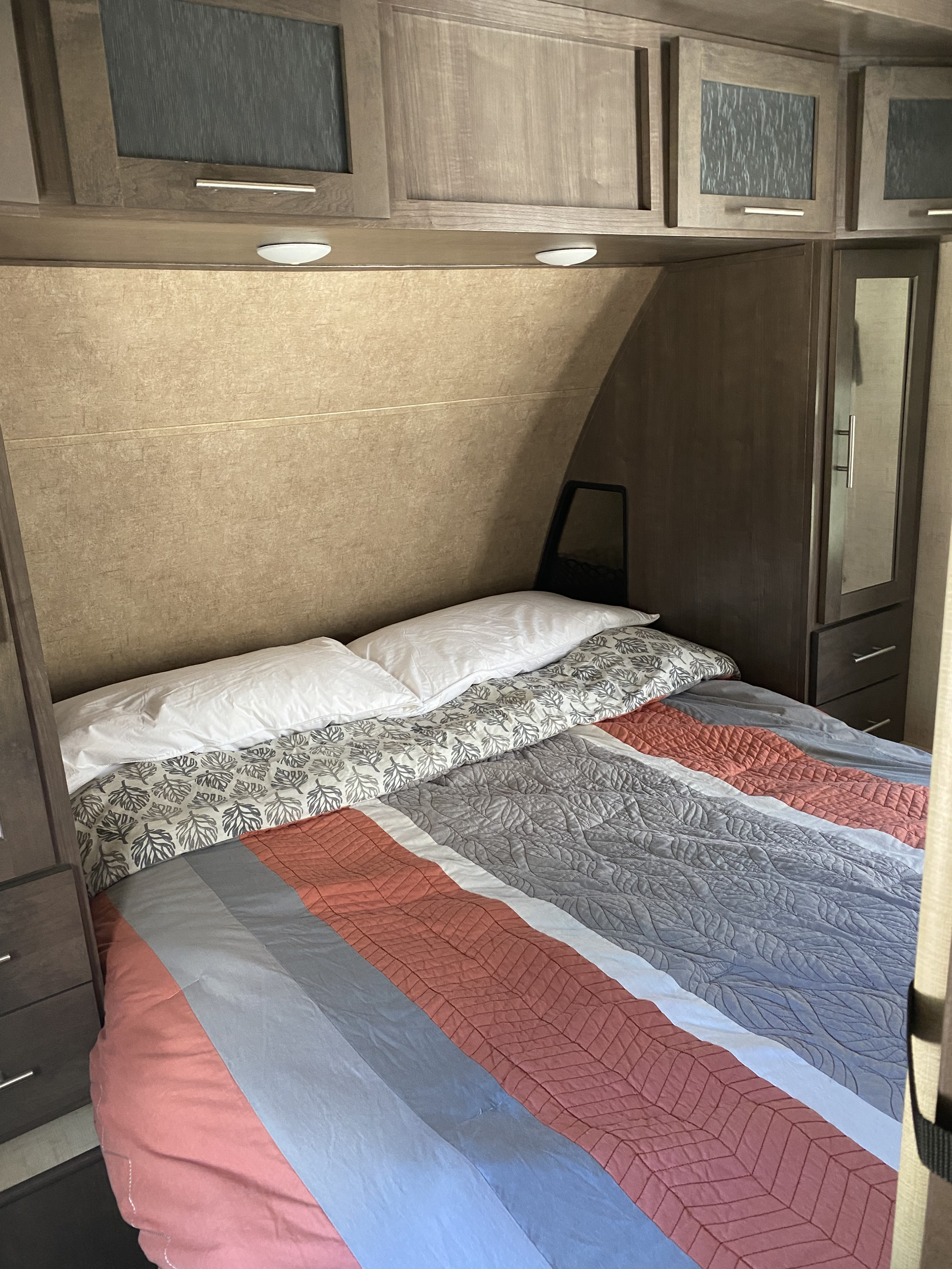 Cozy RV rental bedroom with patterned comforter, overhead cabinets, and wardrobe, ideal for comfortable travel.. Forest River Surveyor 2017