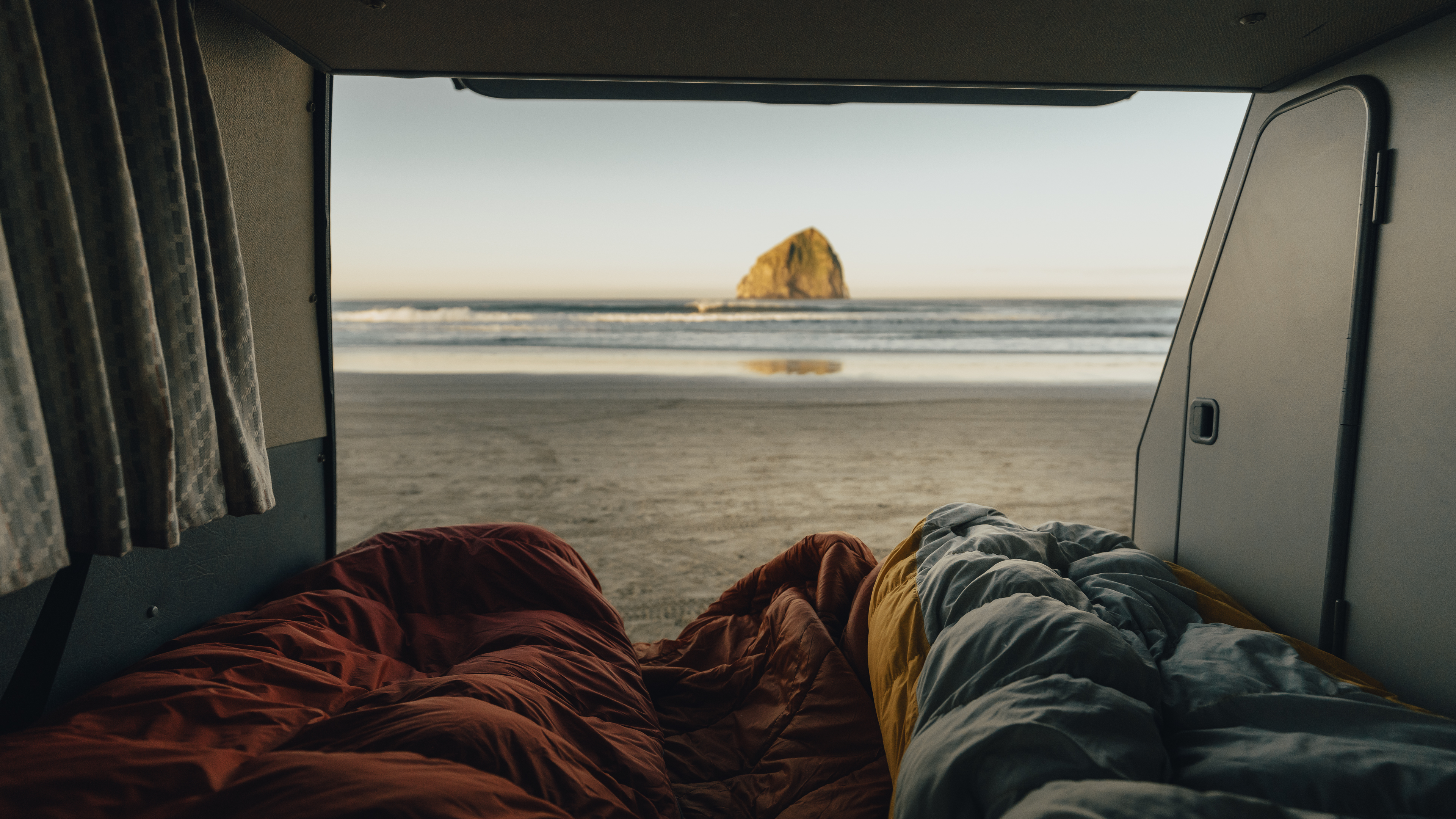 RV rental view: Cozy sleeping bags face a serene beach, ocean, and sea stack. Perfect camper van getaway.. Volkswagen Vanagon 1991