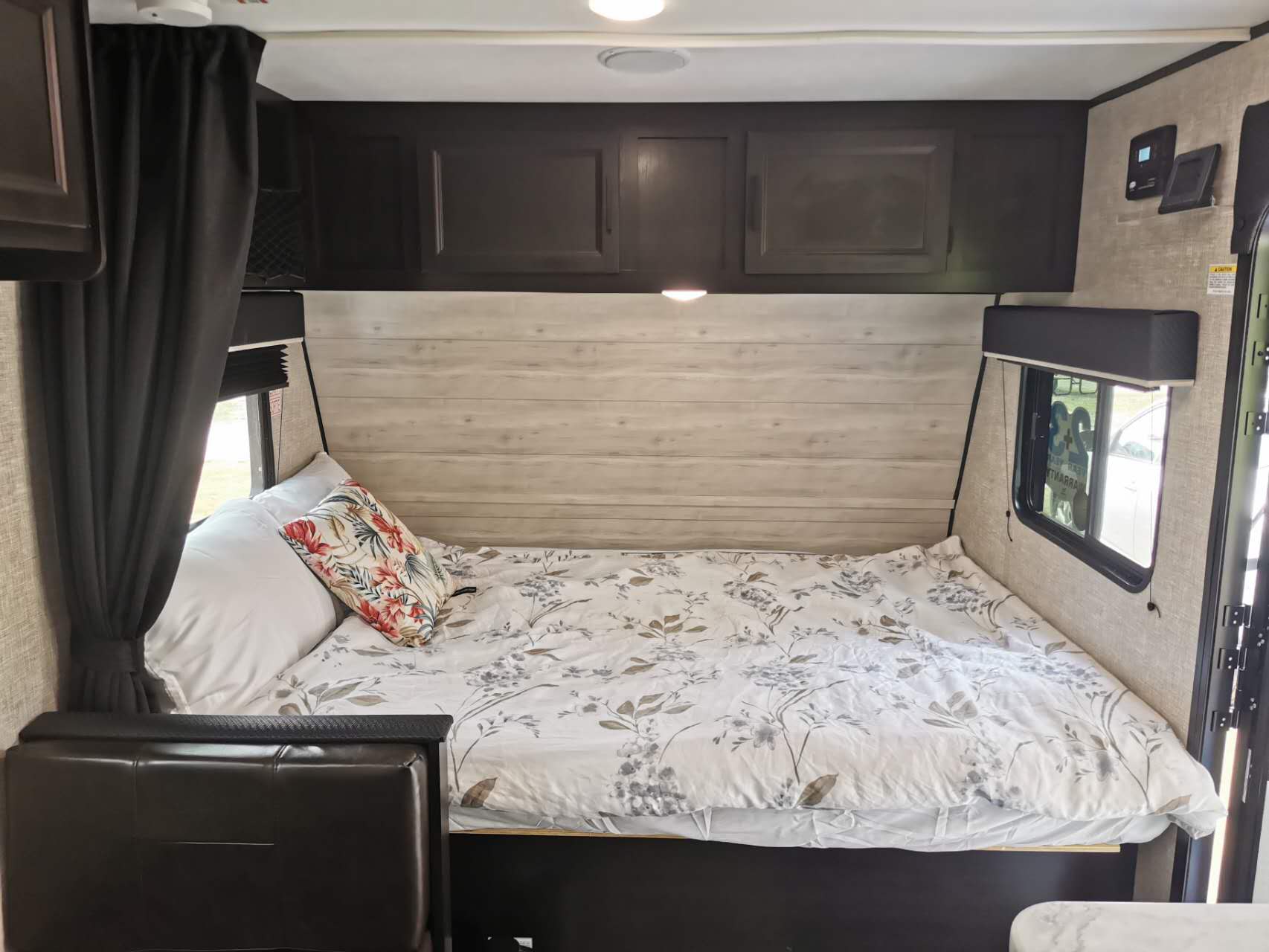 Inside a cozy RV rental bedroom: a comfortable bed with floral bedding, wall paneling, and dark storage cabinets.. Jayco Jay Flight SLX 2022