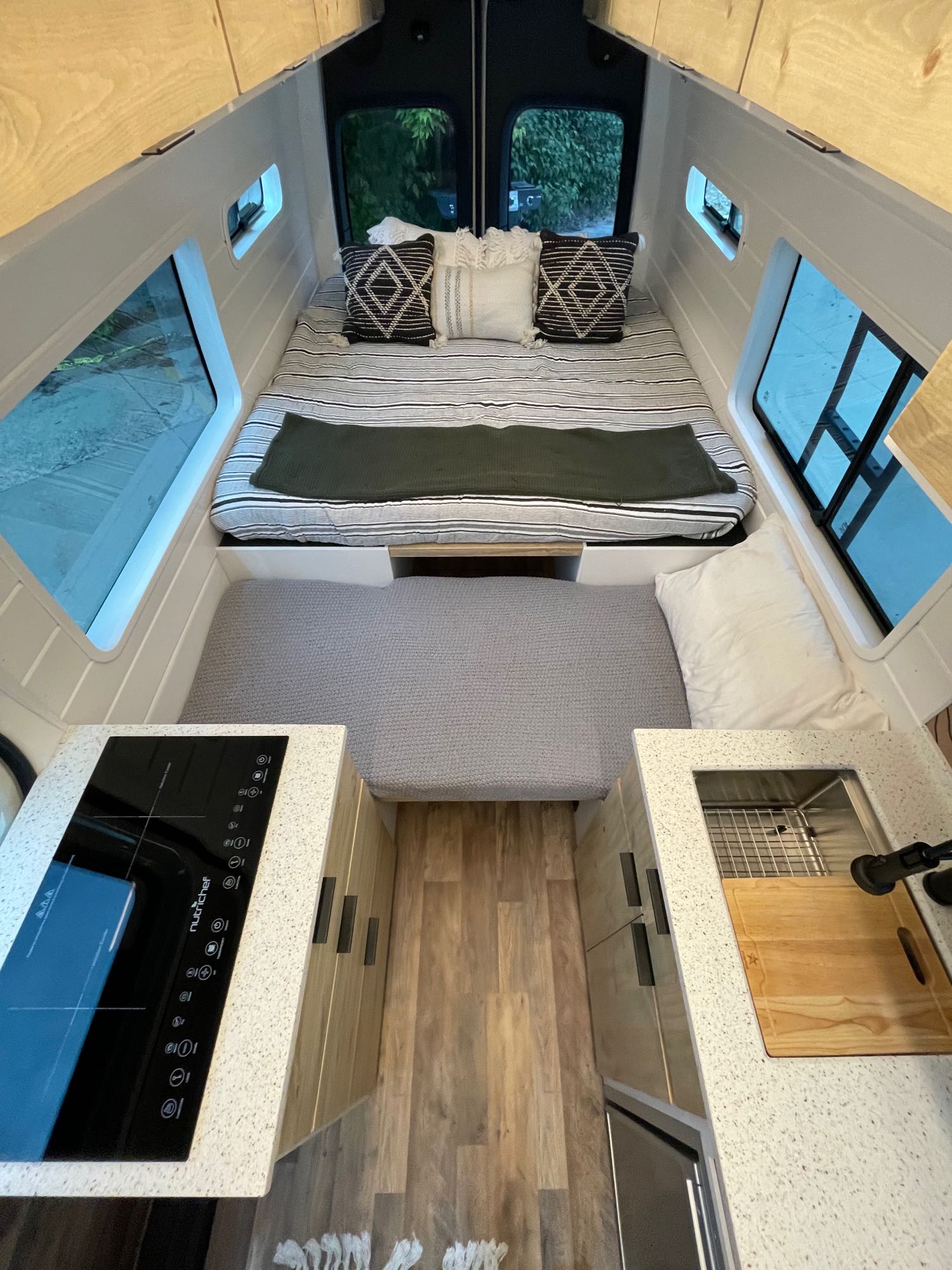This modern RV rental interior offers a rear bed, compact kitchen with stovetop & sink, and versatile bench seating.. Mercedes-Benz Sprinter 419 LWB High Roof 2021