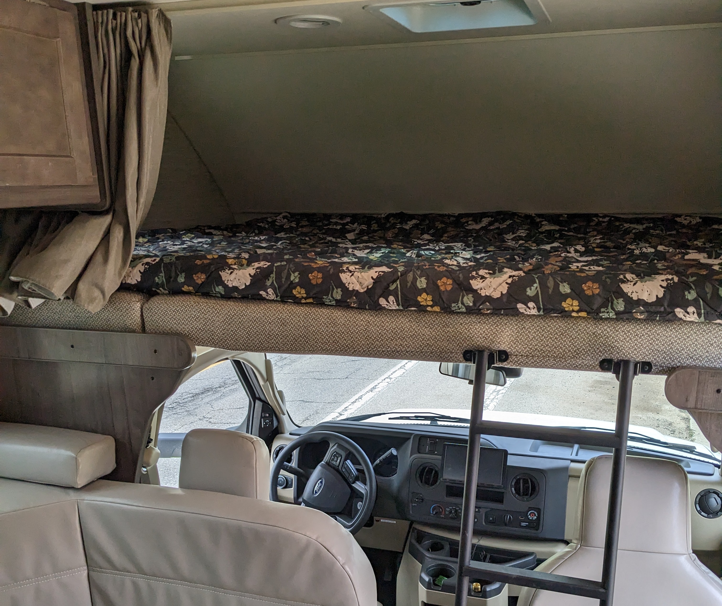 Inside this RV rental: a spacious cab-over bunk with floral bedding above the functional driver's cockpit.. Winnebago Minnie Winnie 2022