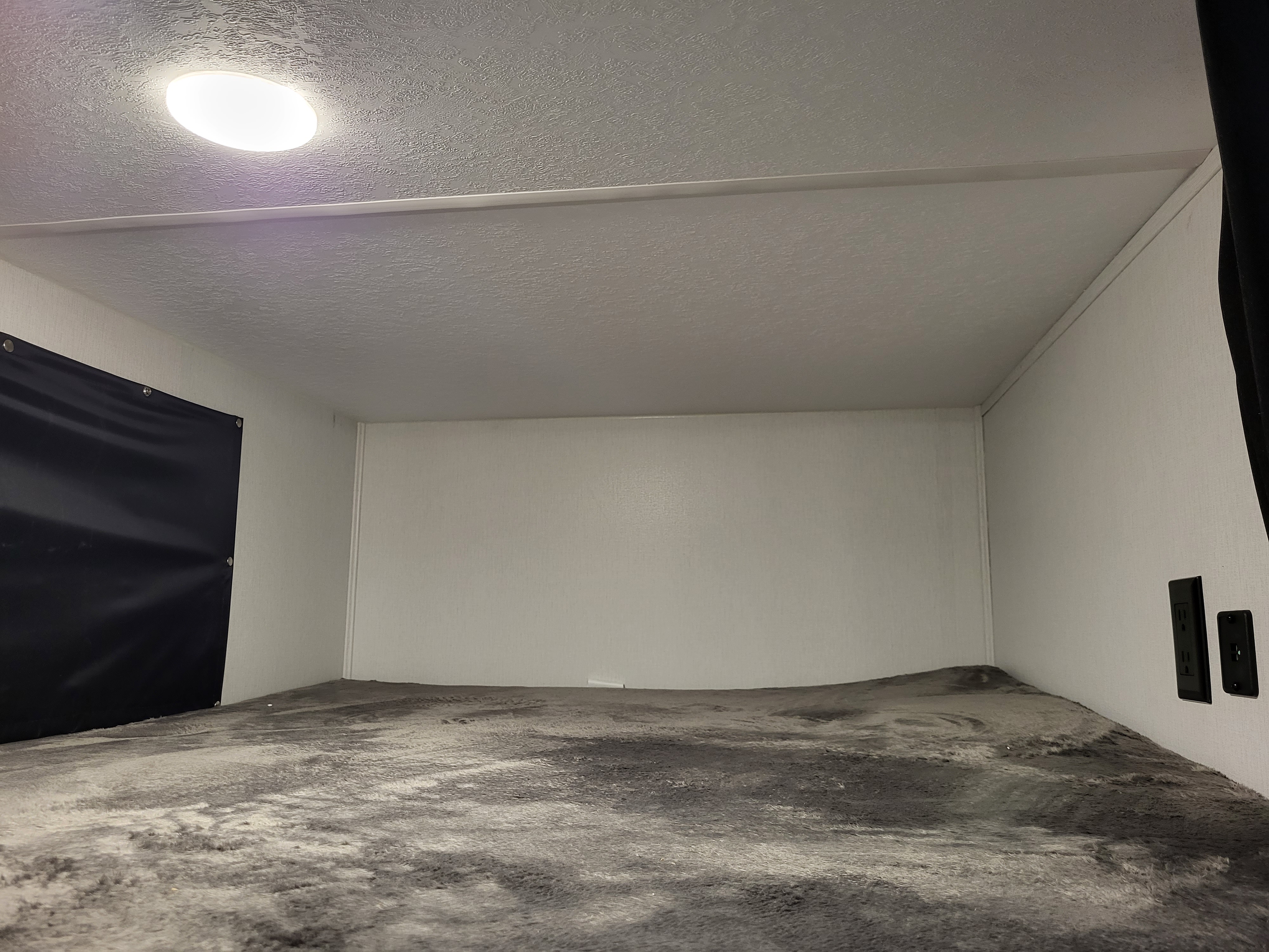 RV rental bunk interior: round ceiling light, textured walls, cozy gray bedding, black curtain, and outlets.. Coachmen Freedom Express Ultra Lite 257BHS 2023