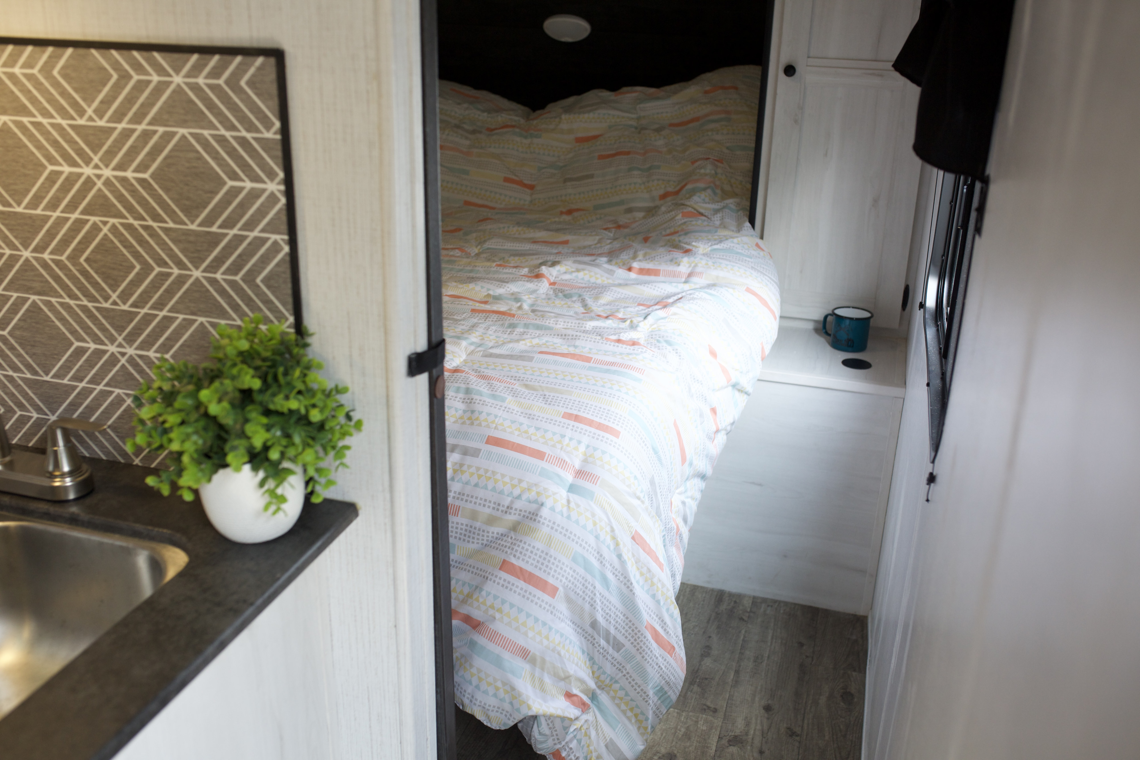 Inside a comfy RV rental: a bright patterned bed in a sleeping nook & compact kitchen counter with sink.. Heartland Trail Runner 2022