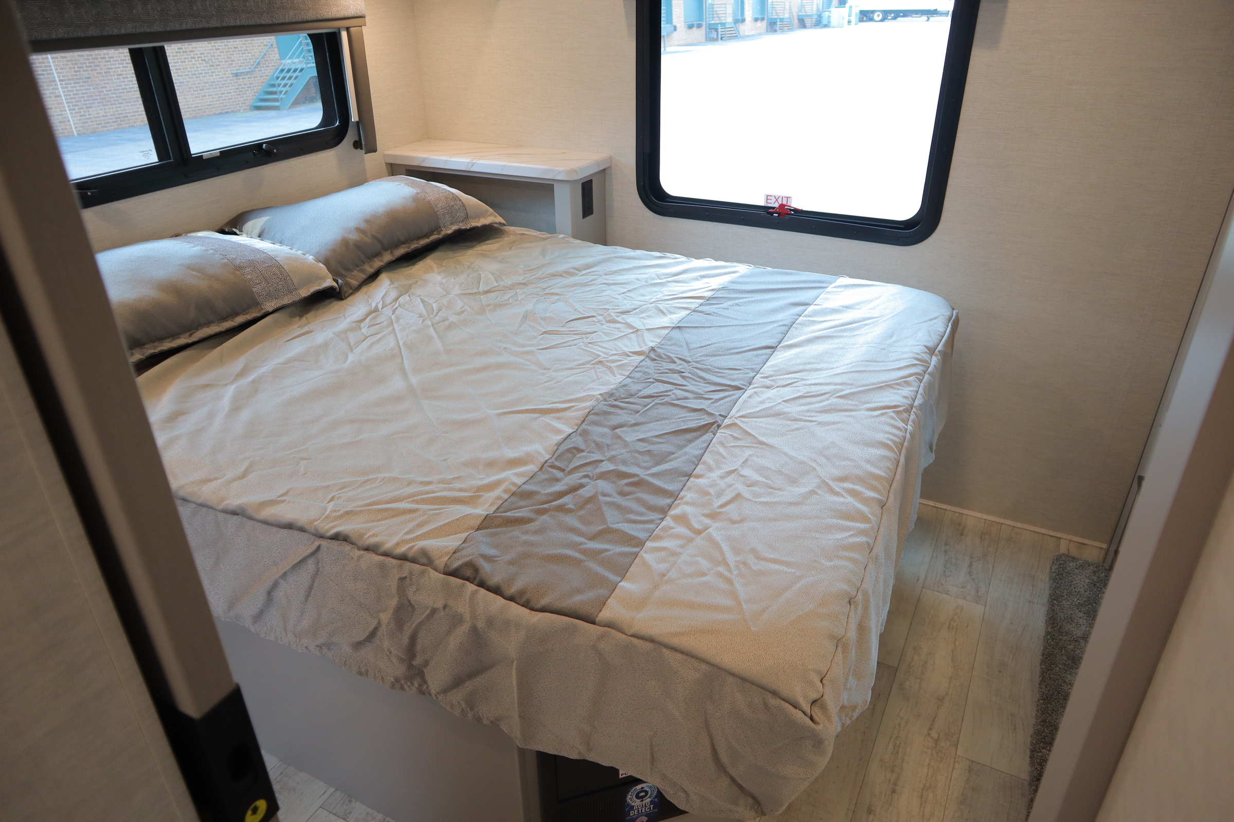 Inside an **RV rental** bedroom, featuring a large bed with neutral-toned bedding, two windows, and a built-in nightstand.. Thor Motor Coach Chateau 2024