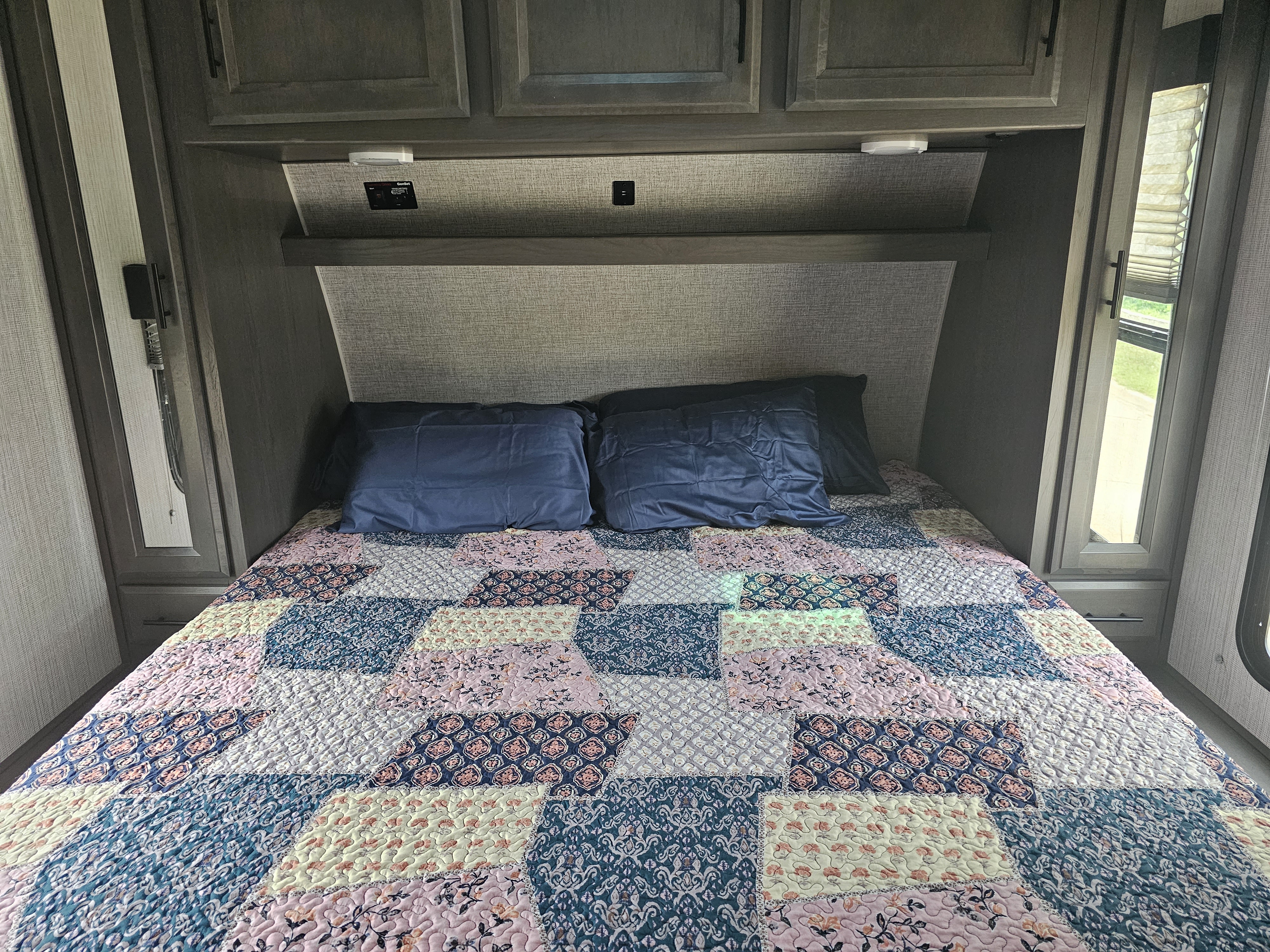 Cozy RV rental bedroom featuring a bed with a vibrant patchwork quilt, dark blue pillows, and built-in storage.. Heartland F-305 Fuel 2021