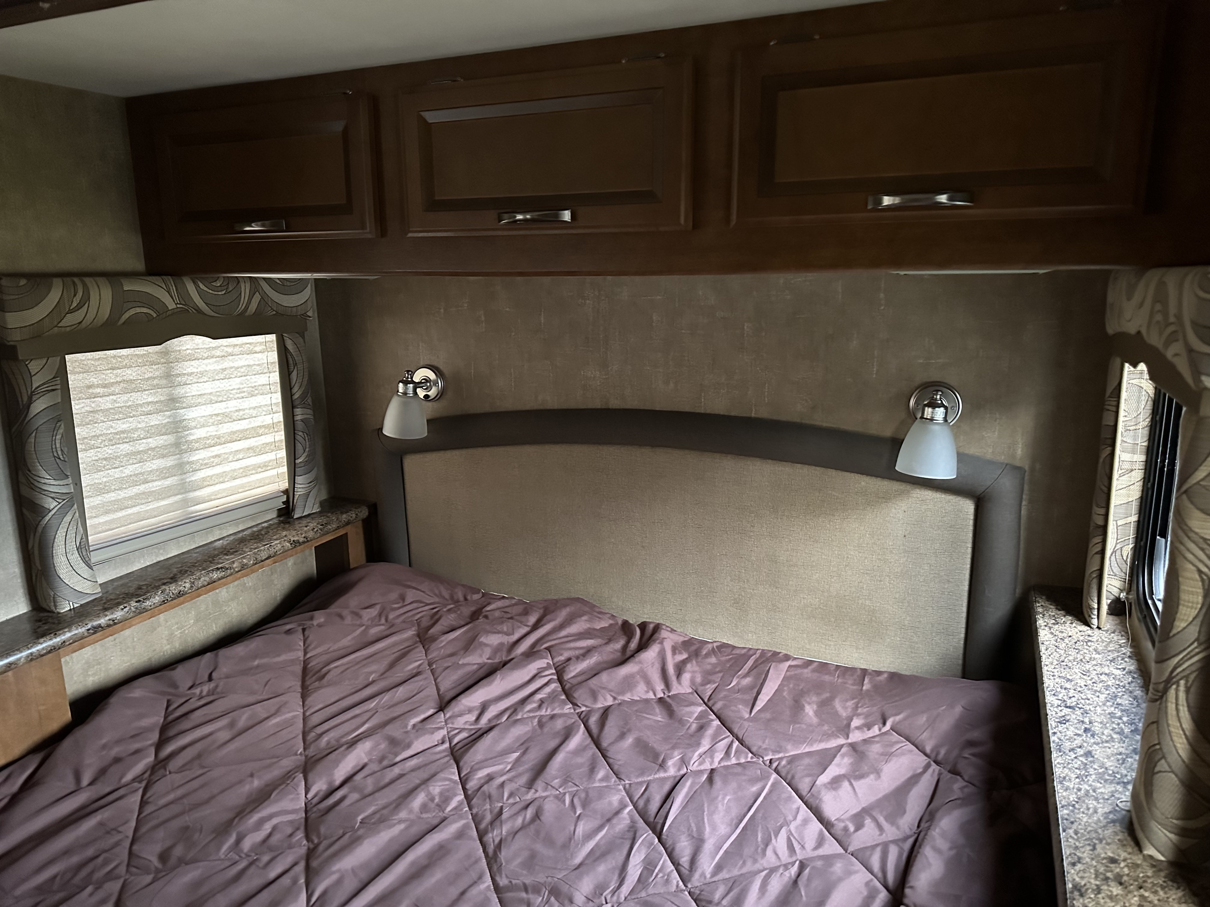 Compact RV rental bedroom with overhead storage, a cozy bed, and wall-mounted lamps, ideal for your next trip.. Thor Chateau 2015