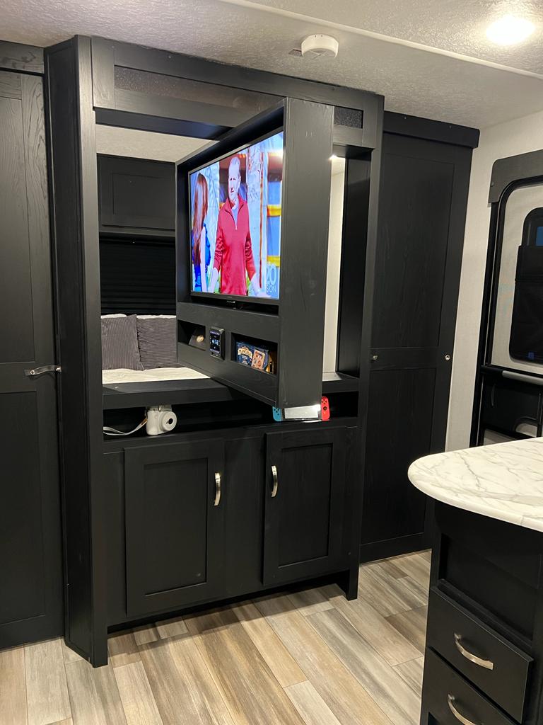 A modern RV rental's living space features a black pop-up TV entertainment unit showing a show, with sleek cabinetry.. Coachmen Freedom Express Ultra Lite 257BHS 2022