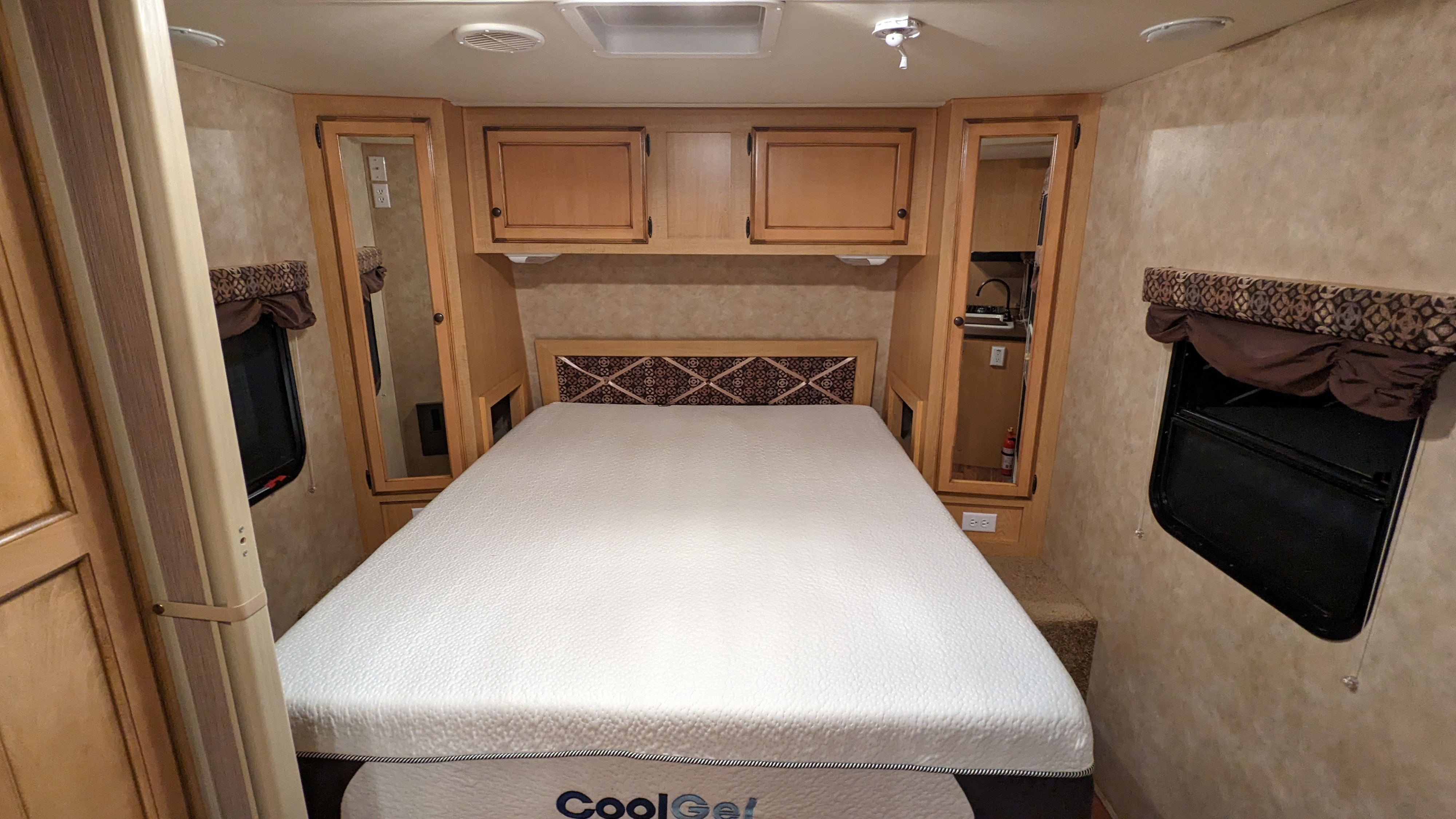 RV rental bedroom: CoolGel mattress, ornate headboard, compact cabinets/sink, and windows. A cozy and functional travel space.. Spree Spree Trailer 2010