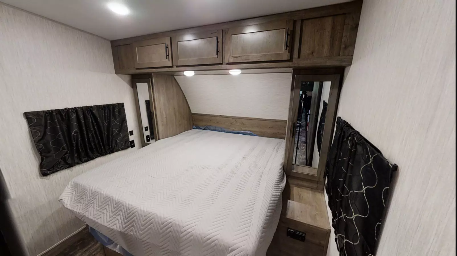 Compact RV rental bedroom featuring a bed with white quilt, wood cabinets, and dark window shades. Comfortable interior.. Forest River Cherokee Wolf Pack 2020